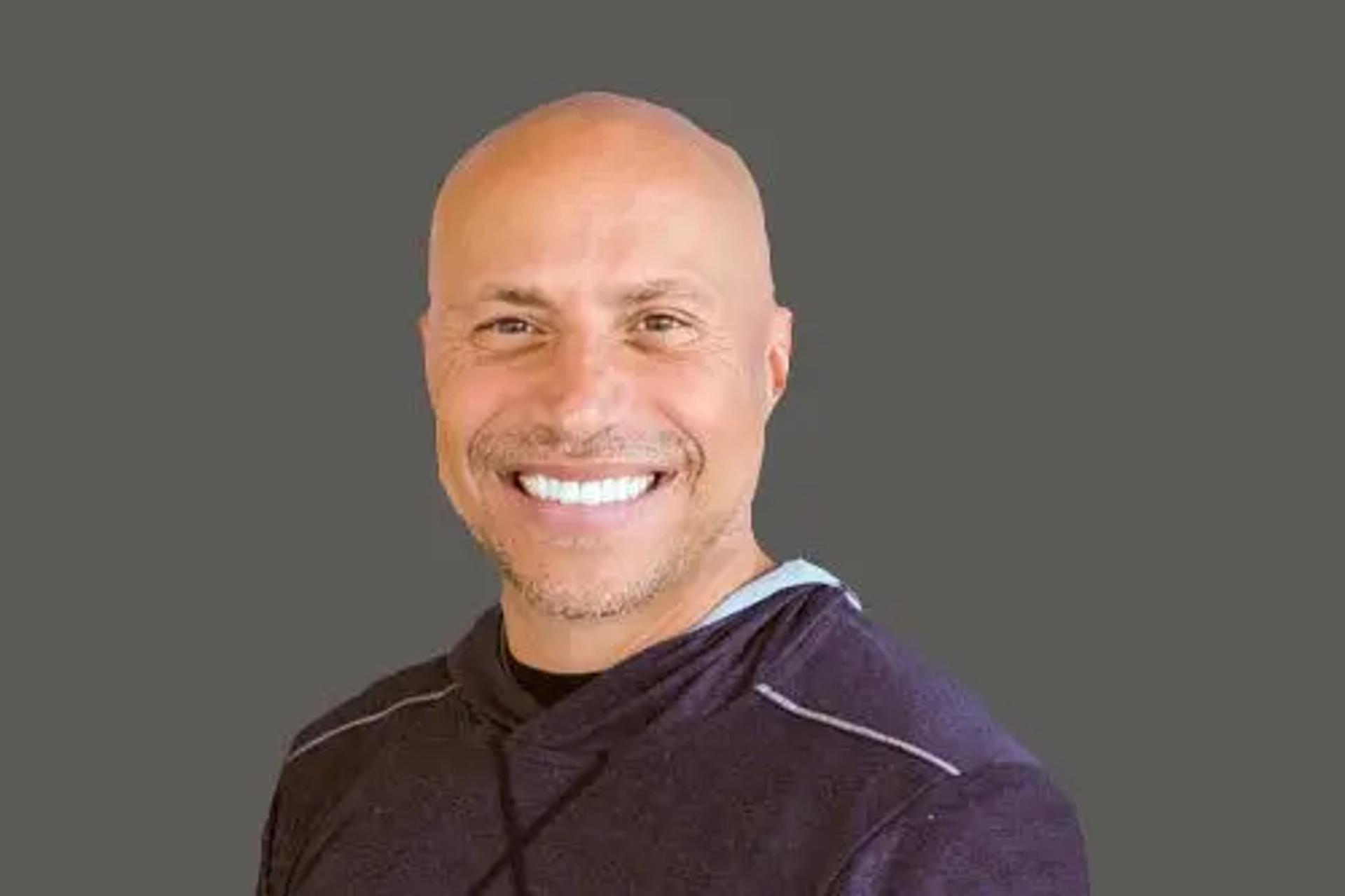 Smiling bald man with a stubble beard in a dark hoodie.