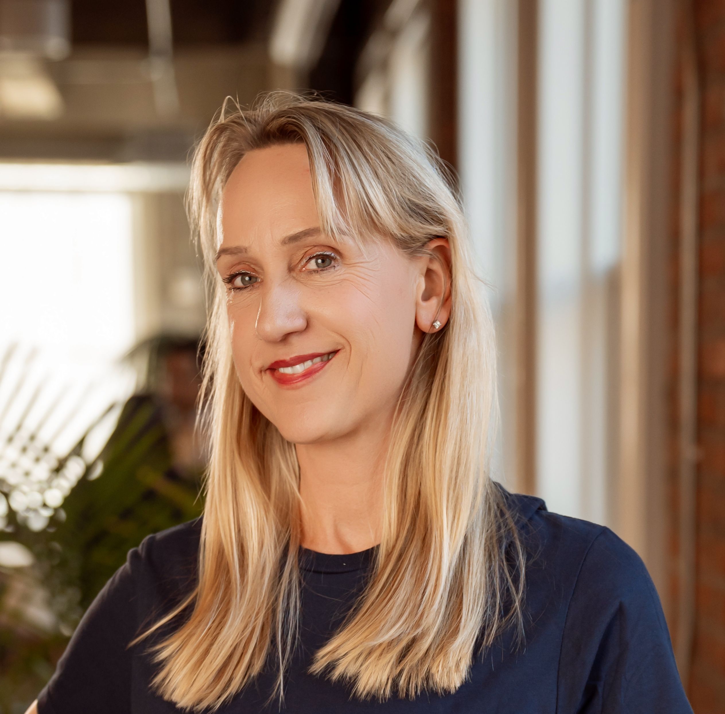 A smiling woman with blonde hair wearing a navy blue shirt.