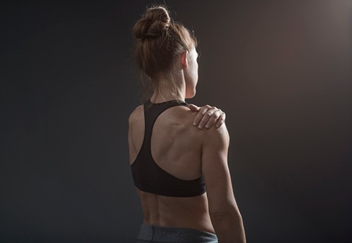 back view of woman holding her shoulder | sore muscles after workout