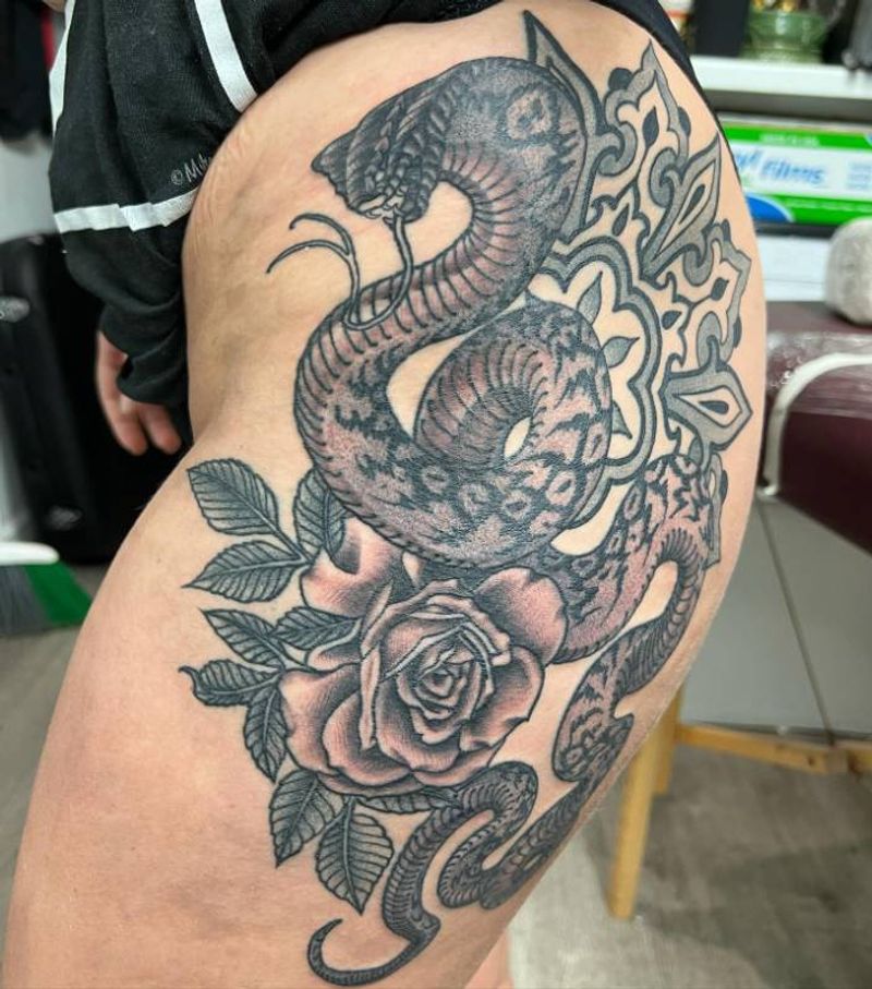 Black and grey illustrative snake and rose tattoo on thigh