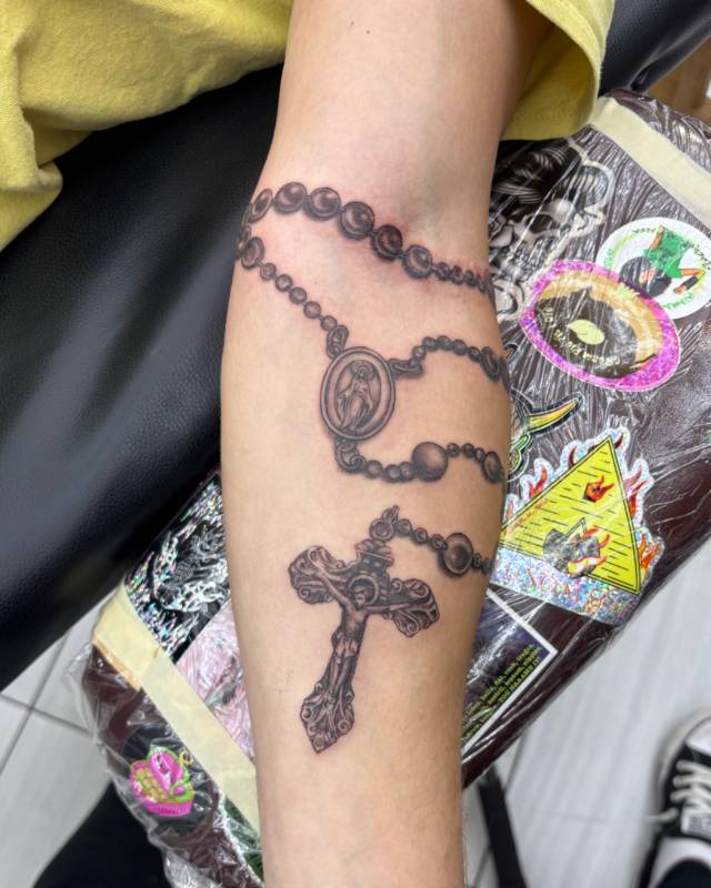 Black and grey realistic rosary tattoo on forearm
