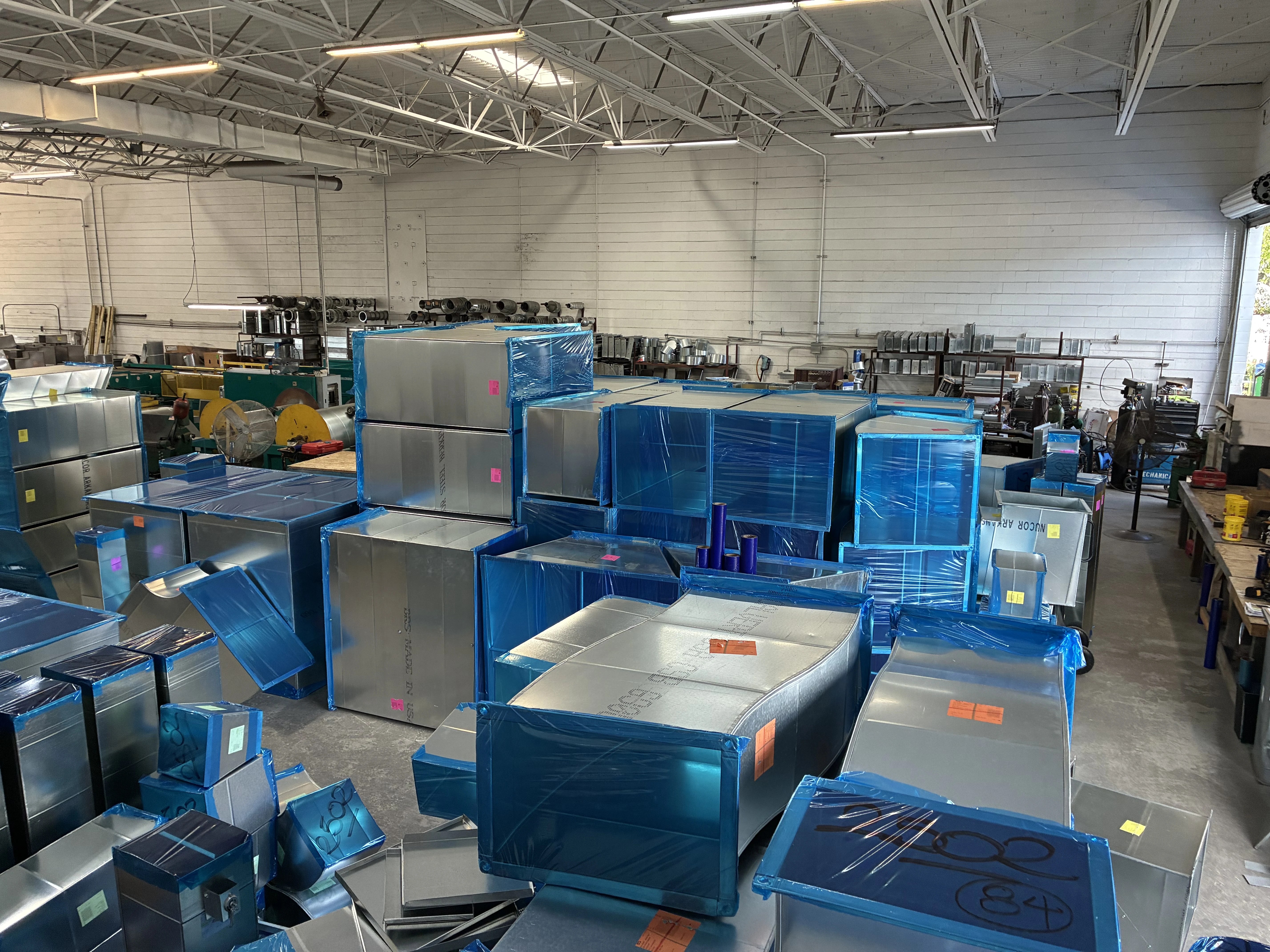 Stacks of fabricated sheet metal ductwork wrapped in protective film on the shop floor