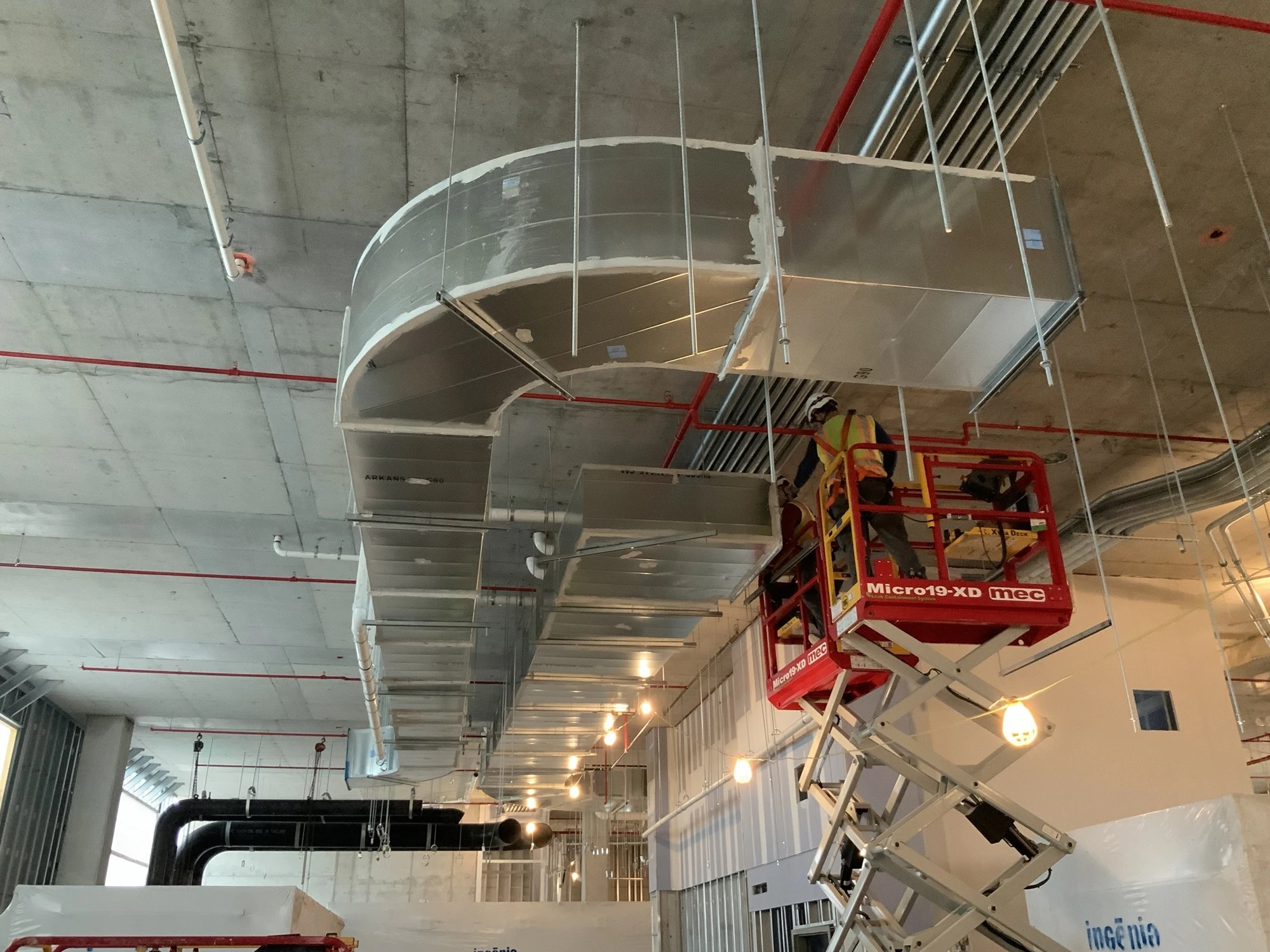 Large rectangular ductwork above a scissor lift in a building under construction at BayCare Manatee