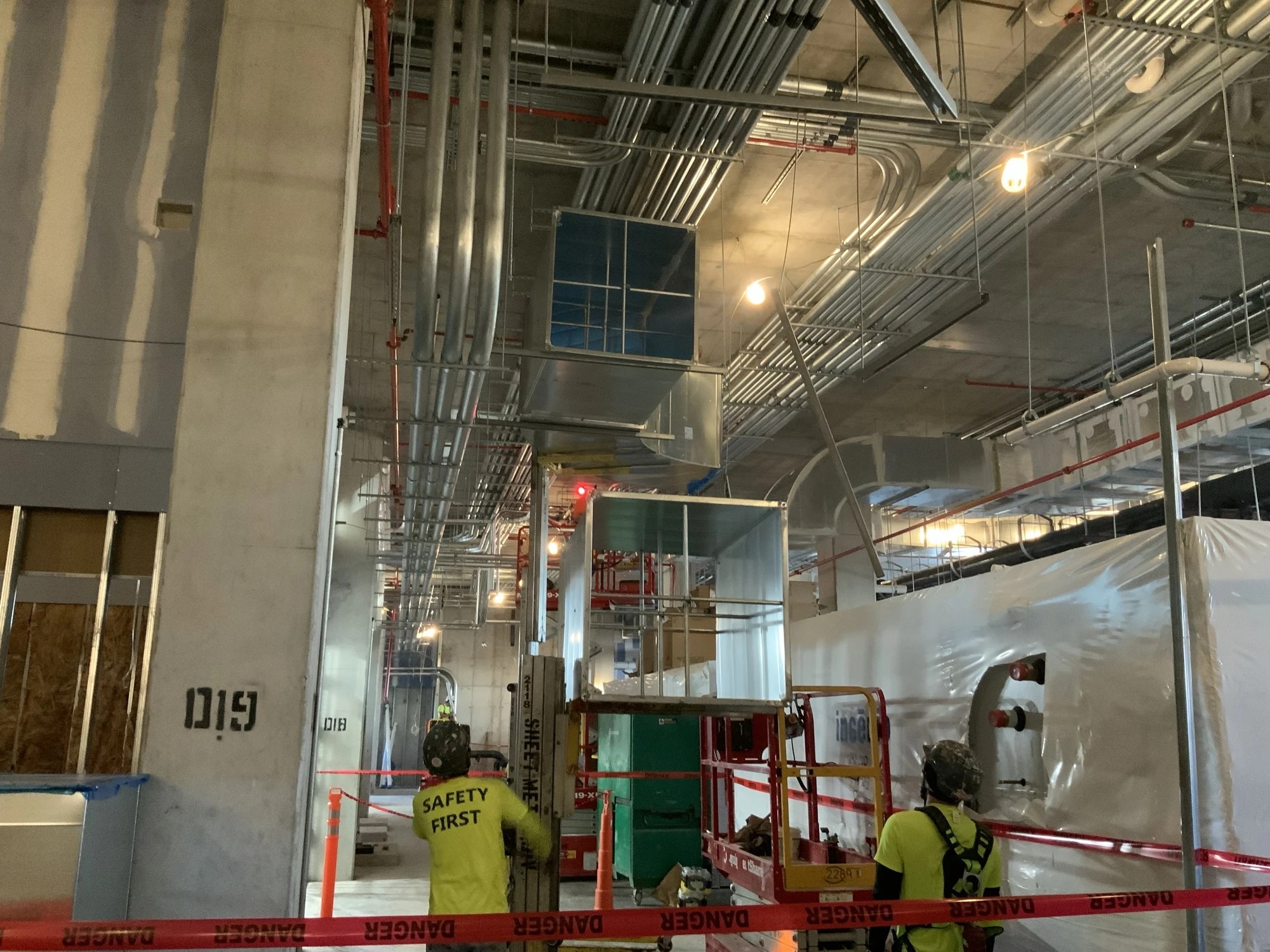 Ductwork, overhead services and construction personnel in an unfinished mechanical space at BayCare Manatee