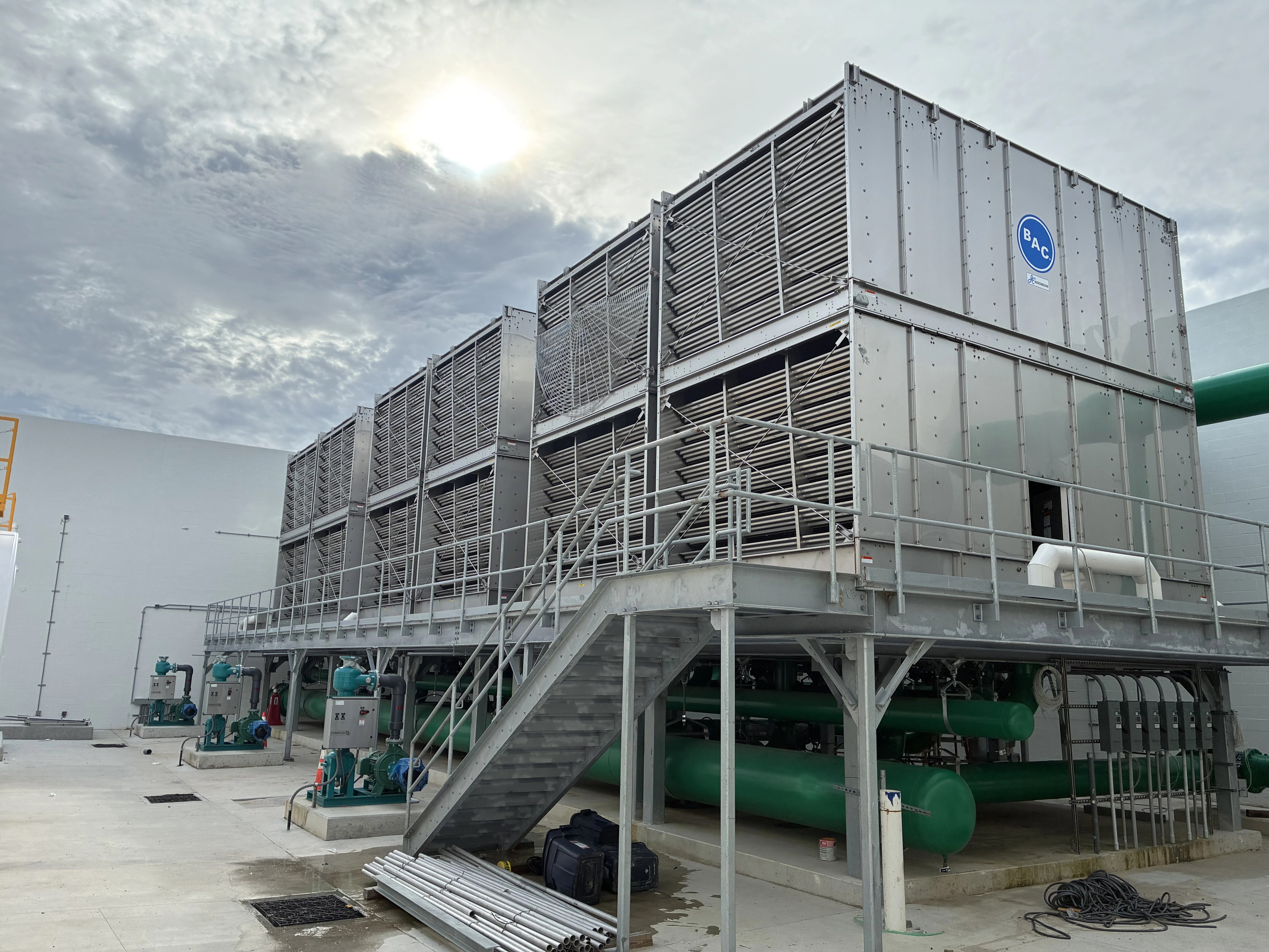 Cooling towers on an elevated steel platform with green condenser water piping and pumps below