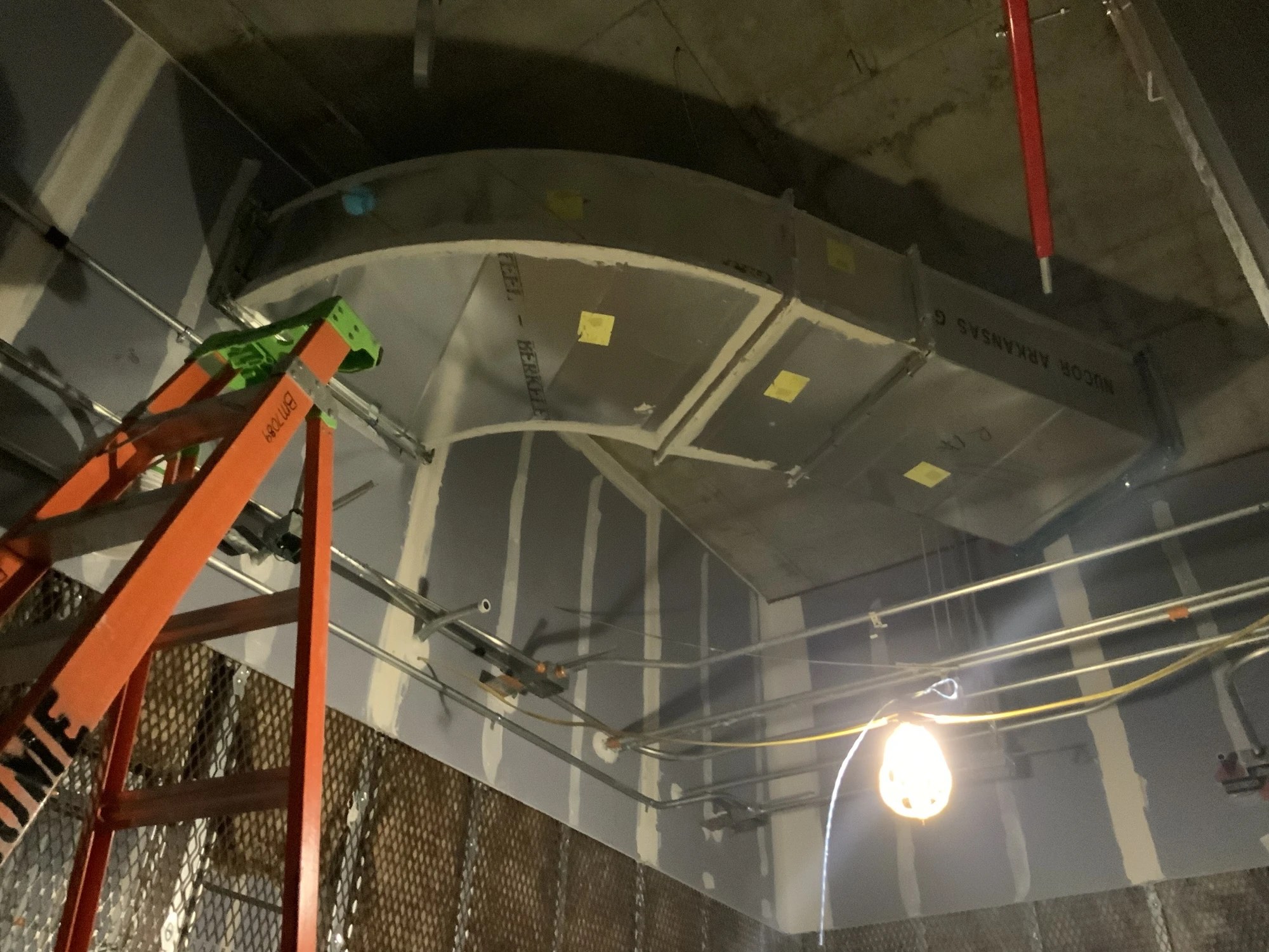 Large curved sheet metal ductwork suspended below a concrete ceiling during construction at BayCare Manatee