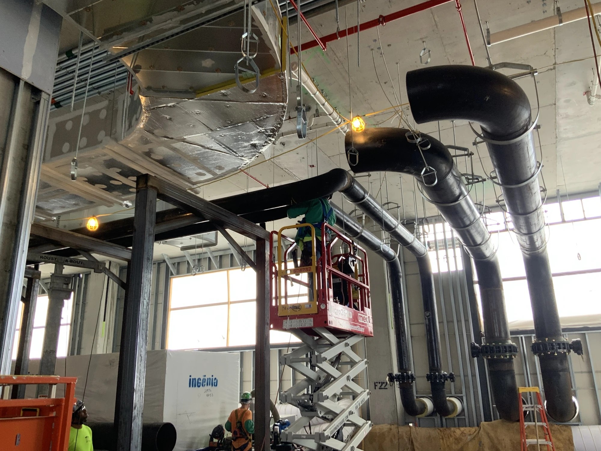 Construction personnel working beside large black piping and overhead sheet metal ductwork at BayCare Manatee