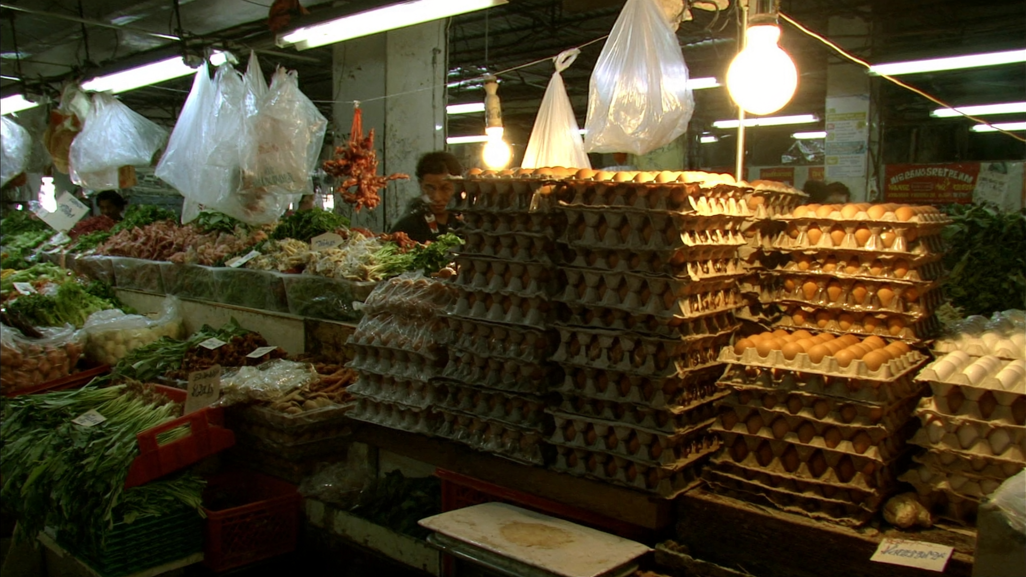 Gerai barangan basah di pasar pagi Malaysia dengan dulang telur dan sayur-sayuran tersusun di bawah lampu gerai