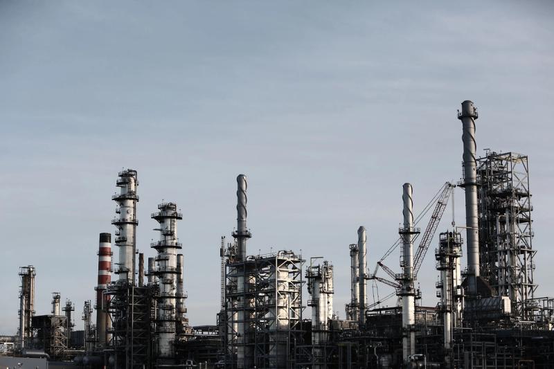 Loji penapisan minyak pada waktu senja, mencerminkan kebergantungan ekonomi pada tenaga dan harga global.