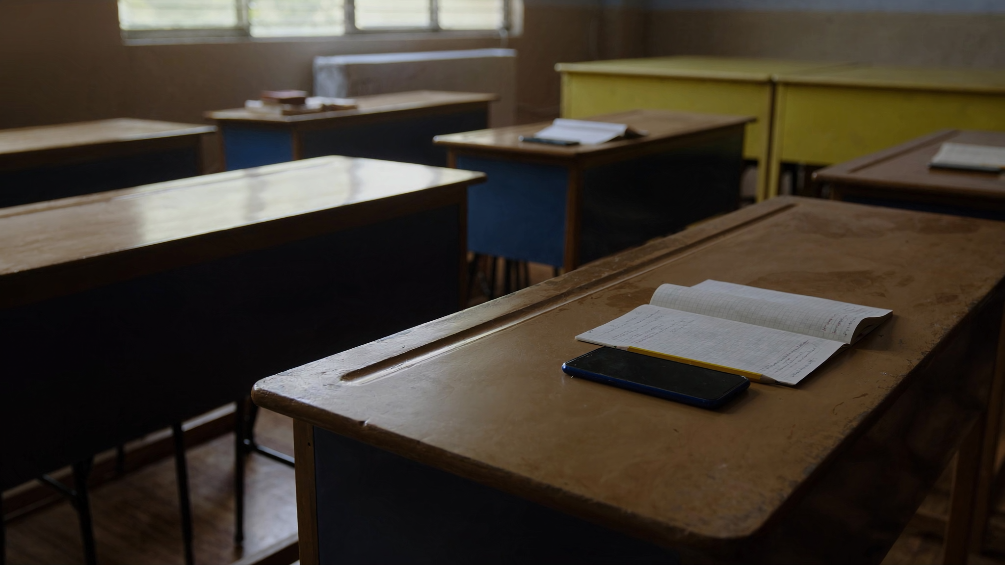 Telefon pintar diletakkan terbalik di atas meja kayu sekolah di sebelah buku latihan dan pensel