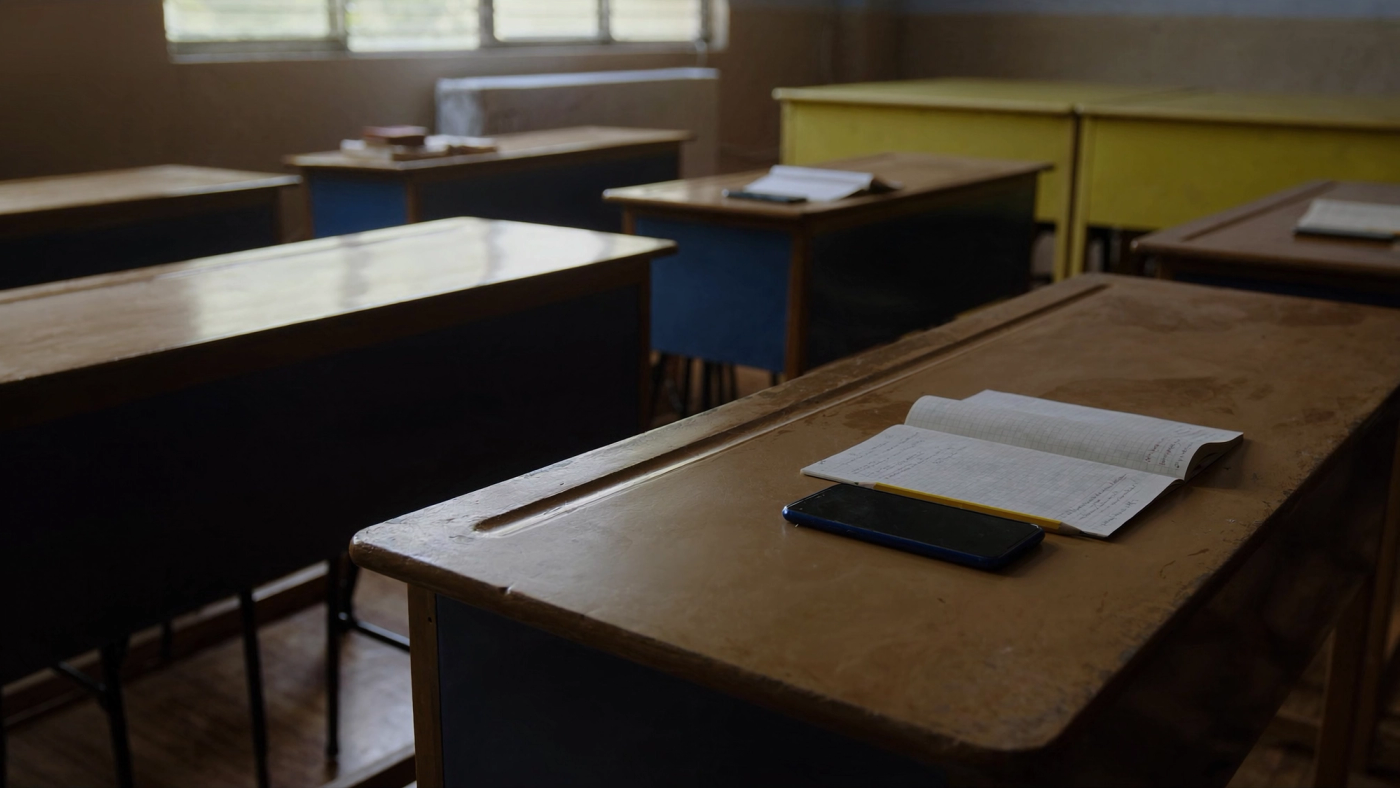 Telefon pintar diletakkan terbalik di atas meja kayu sekolah di sebelah buku latihan dan pensel