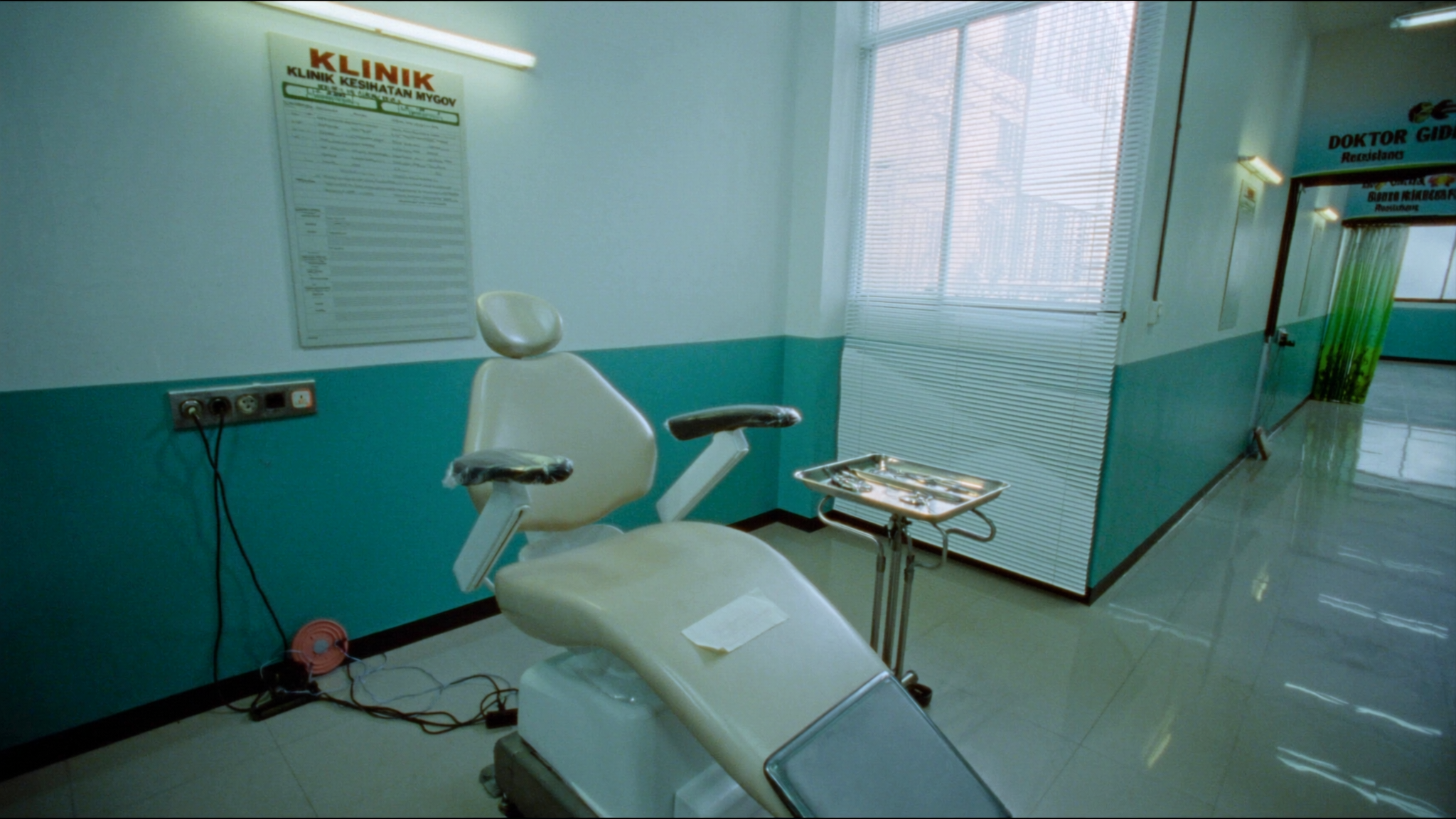 Kerusi rawatan pergigian kosong di sebuah klinik kesihatan kerajaan, dengan dulang instrumen keluli di sisinya