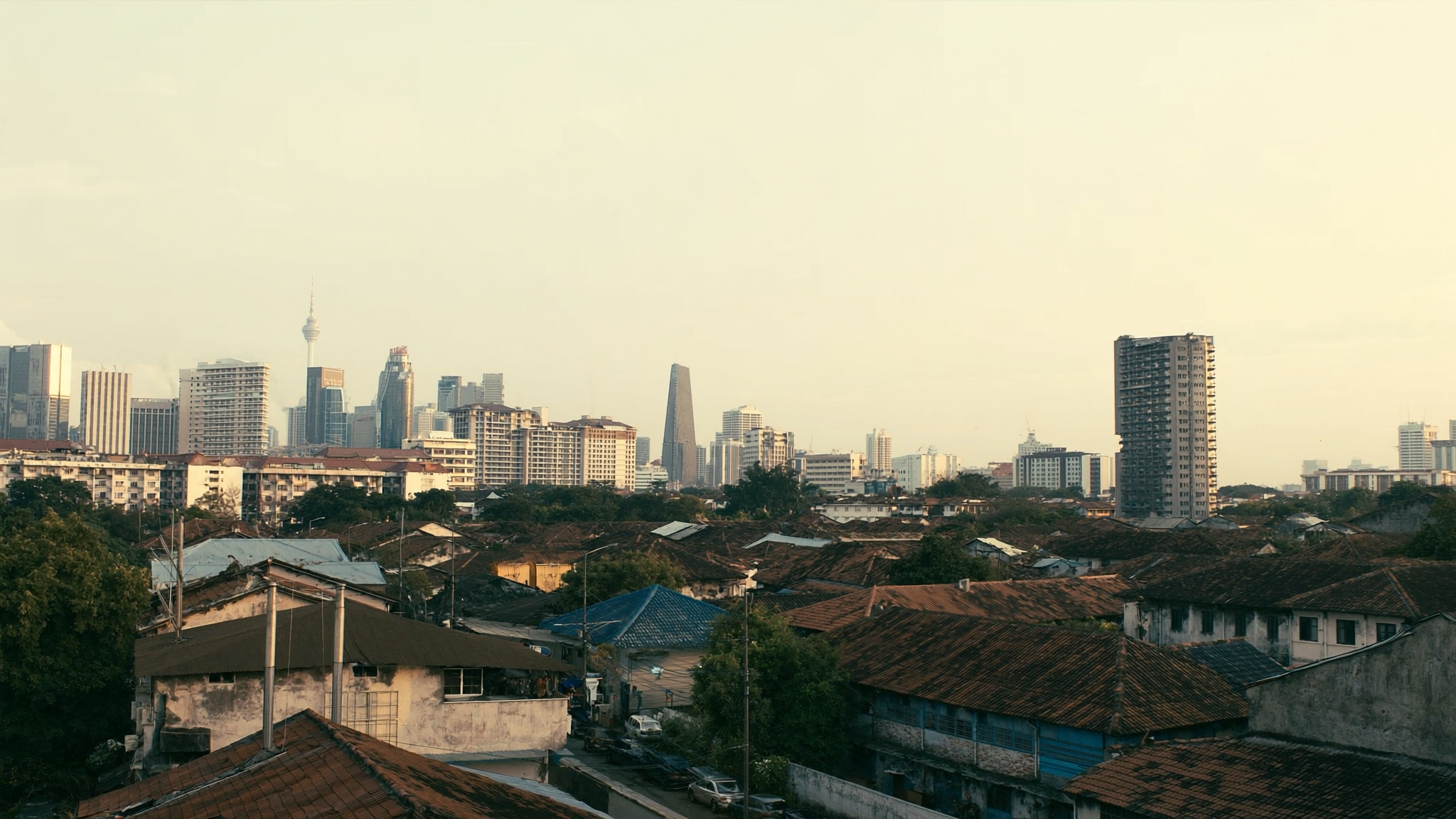 Bumbung rumah teres di pinggir Lembah Klang dengan menara pejabat Kuala Lumpur di kejauhan ketika senja