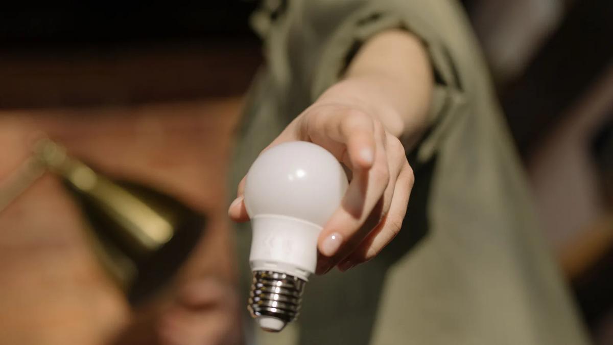 一隻手拿著白色 LED 燈泡，背景是室內居家環境