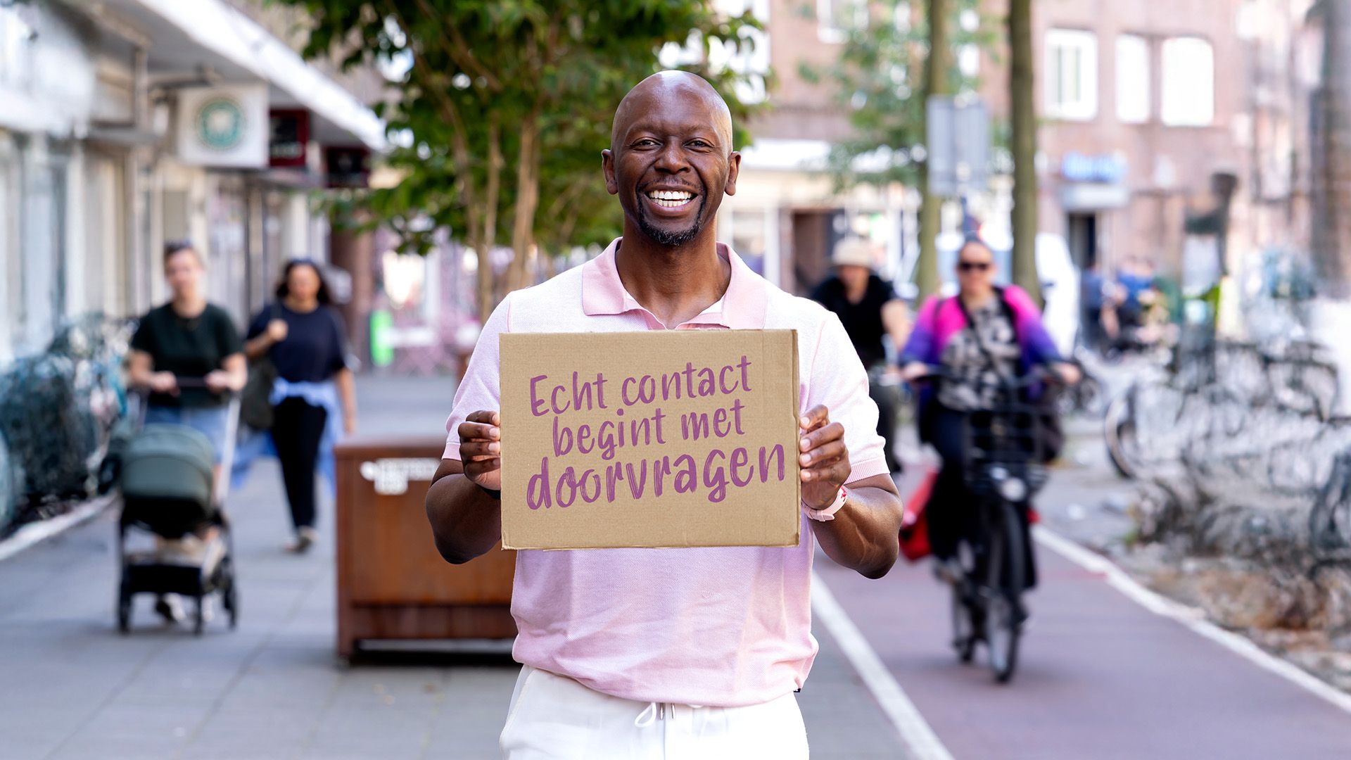 Ben staat buiten met een bord met de Quote "Echt contact begint met doorvragen"