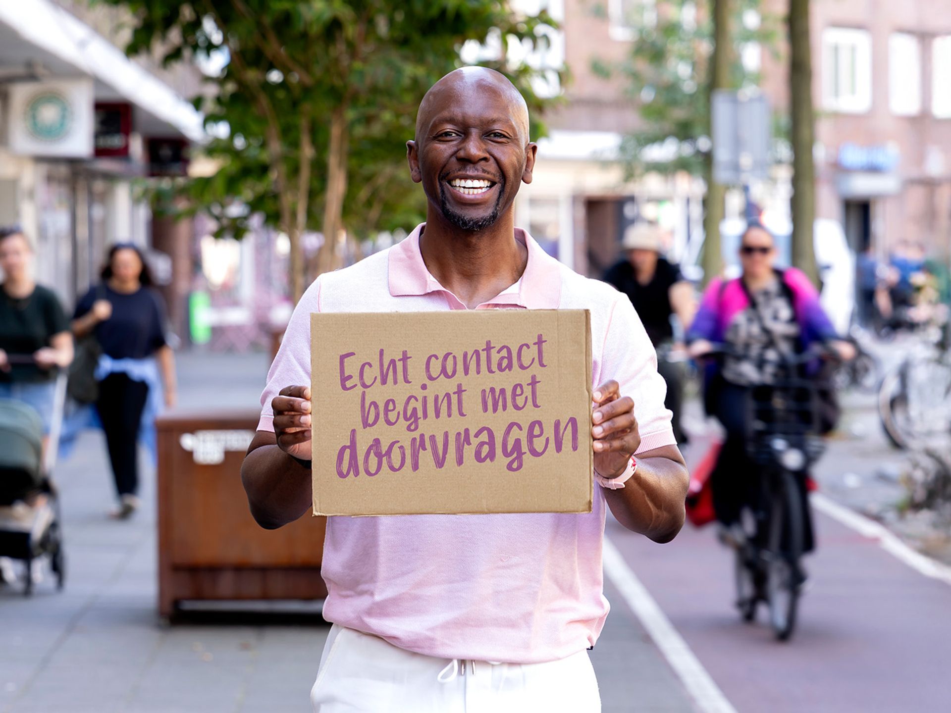 Ben staat buiten met een bord met de Quote "Echt contact begint met doorvragen"