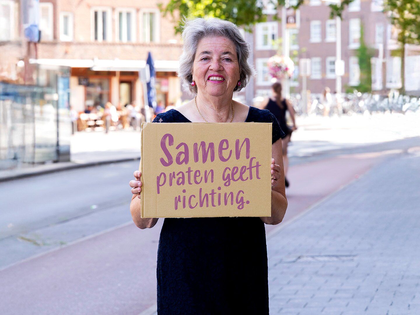 Denise staat buiten met een bord met de Quote "Samen praten geeft richting"