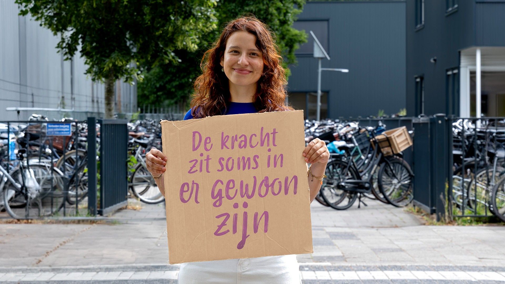 Margit houdt een bord vast met de quote ‘De kracht zit soms in er gewoon zijn’