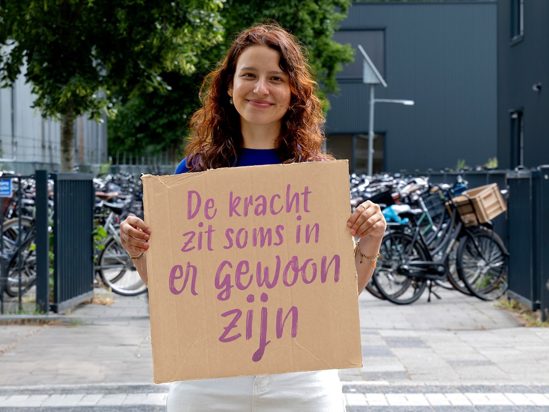 Margit houdt een bord vast met de quote ‘De kracht zit soms in er gewoon zijn’