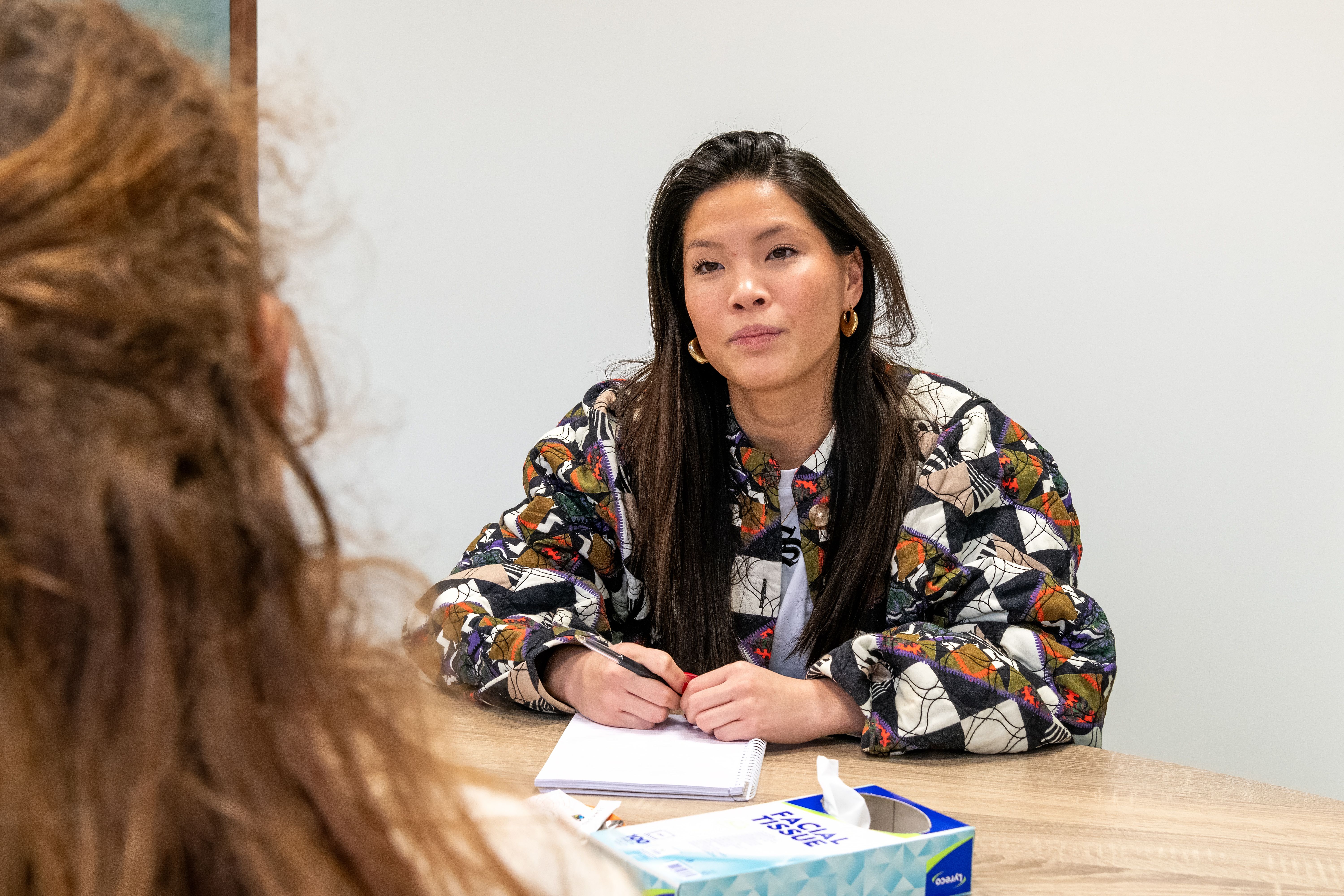 vrouw zit aan tafel en kijkt in camera