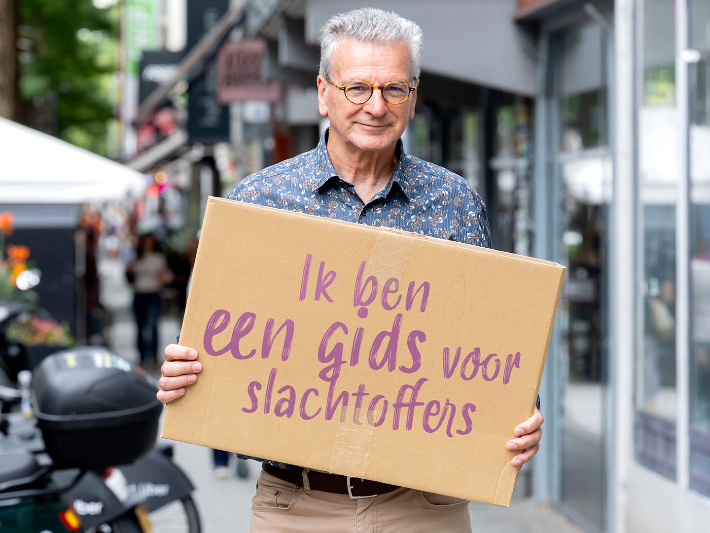 Vrijwilliger Tom houdt een bord op met quote: "Ik ben een gids voor slachtoffers"