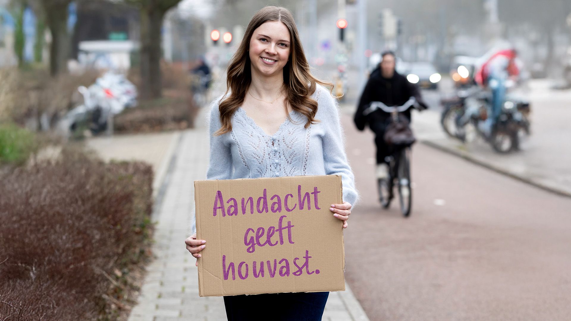 Claire staat buiten met bord in de hand waar op staat: Aandacht geeft houvast