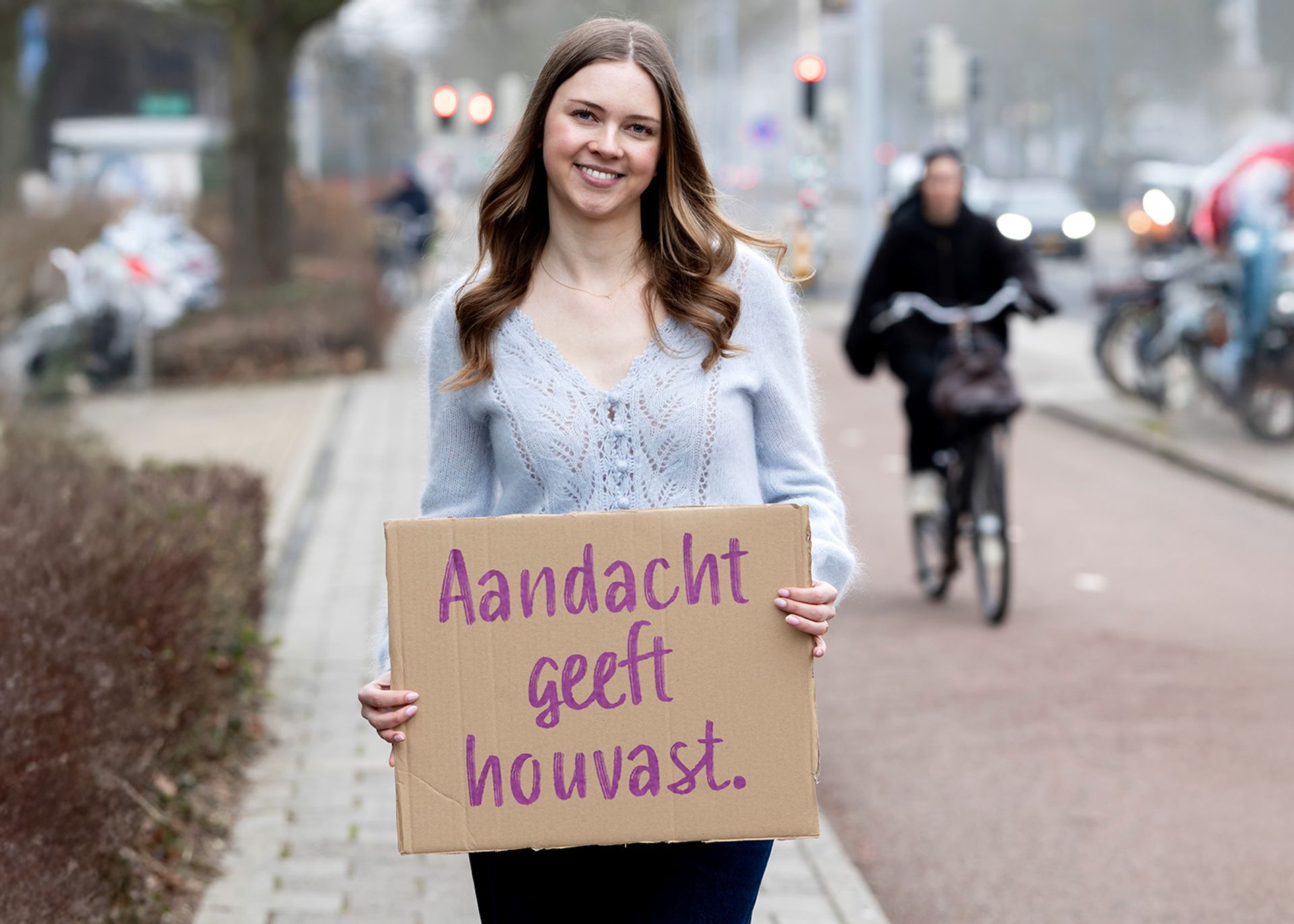 Claire staat buiten met bord in de hand waar op staat: Aandacht geeft houvast