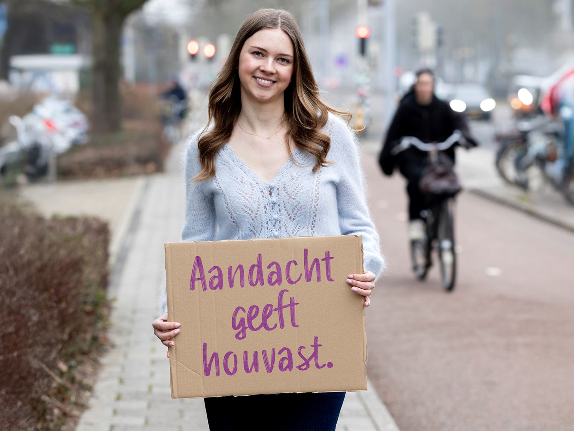 Claire staat buiten met bord in de hand waar op staat: Aandacht geeft houvast