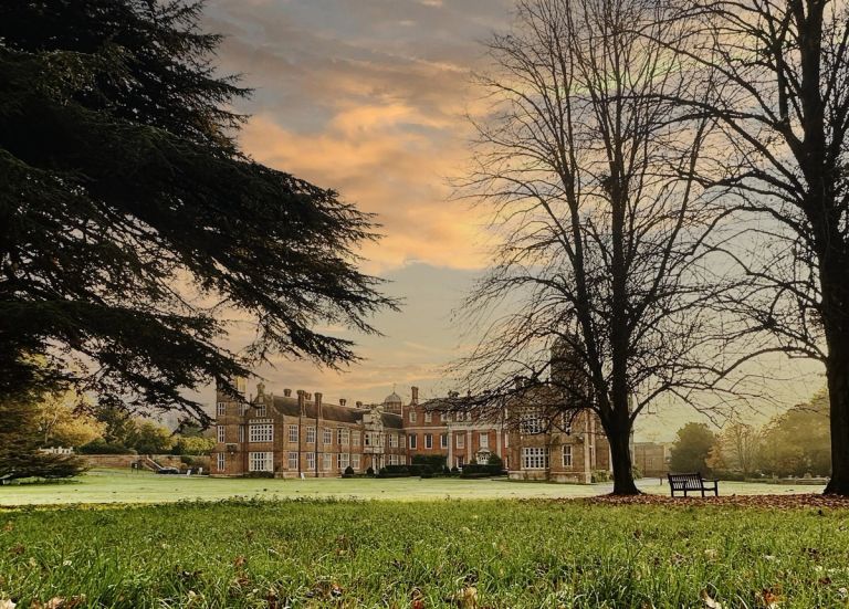 Cobham Hall School with autumn trees, a bench, and cloudy sunset sky, surrounded by a large grassy area.