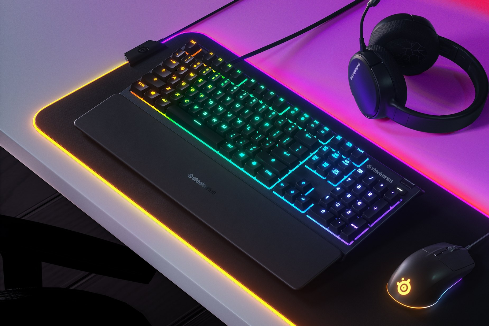 A Steelseries keyboard, headset and mouse appear backlit by a neon pink light