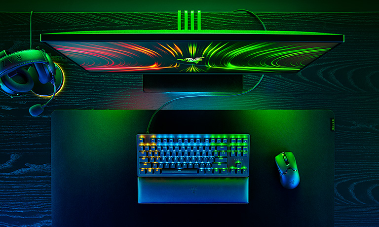 A razer monitor, mouse, headset and keyboard are seen from above at a birds eye view