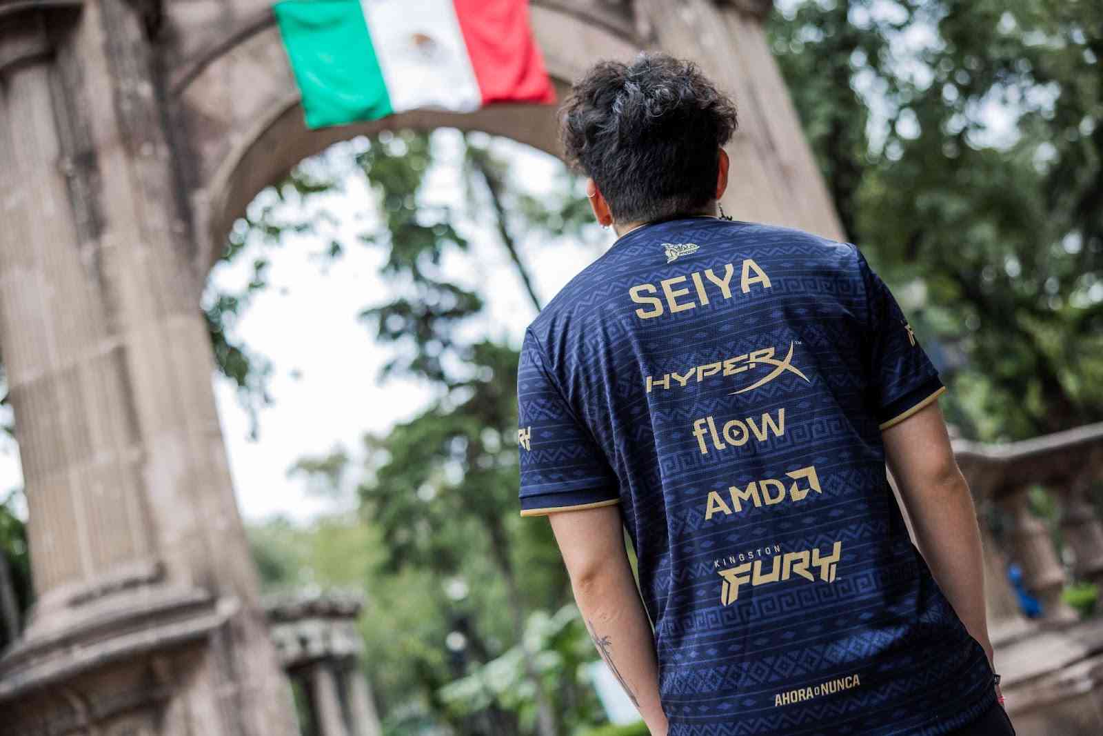 Isurus Gaming's Seiya is pictured from behind with his hands in his pockets wearing his team jersey with his tag and sponsors visible on the back.