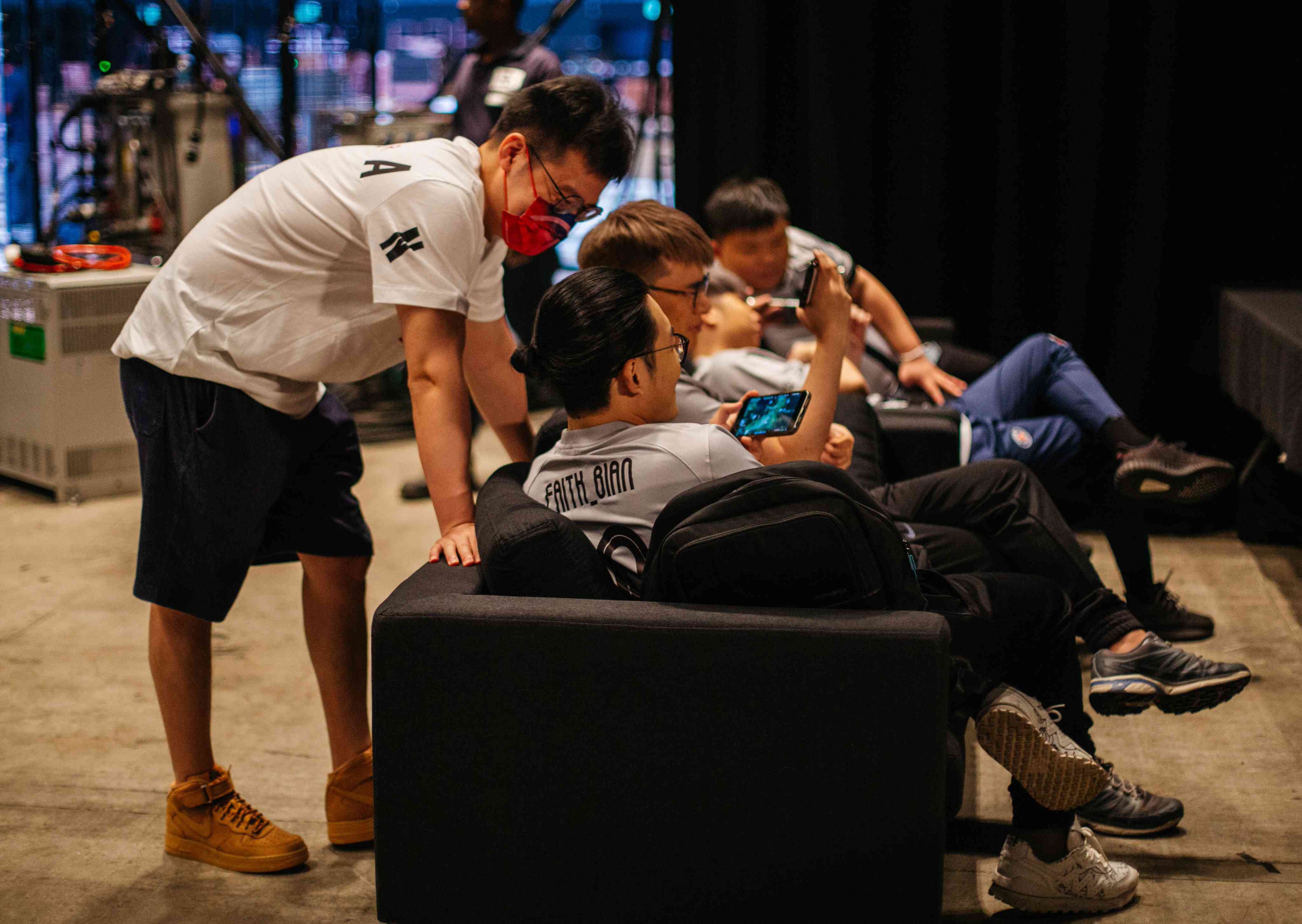 Players from LGD seated on couches backstage on photo day at TI 11, watching and discussing Dota 2 replay videos on their phones