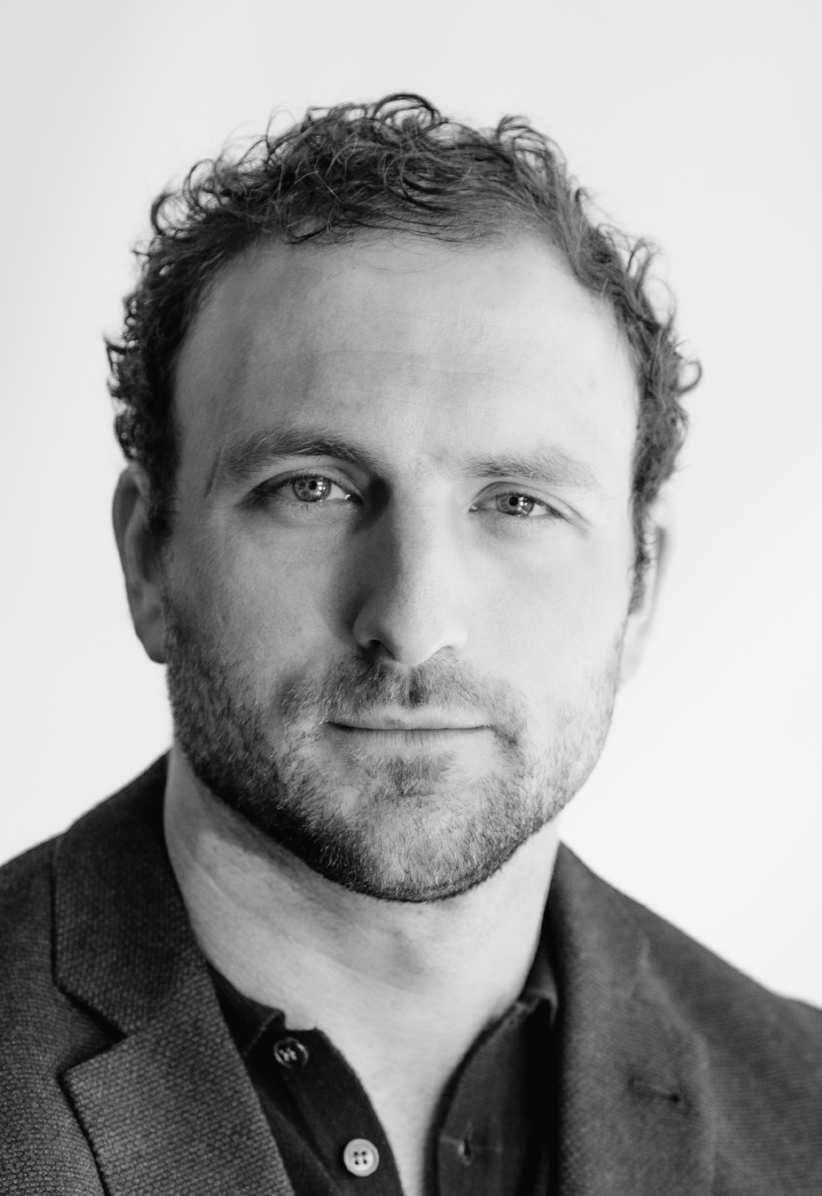 Portrait of Sam Allgood in a blue blazer against a white sunny background.