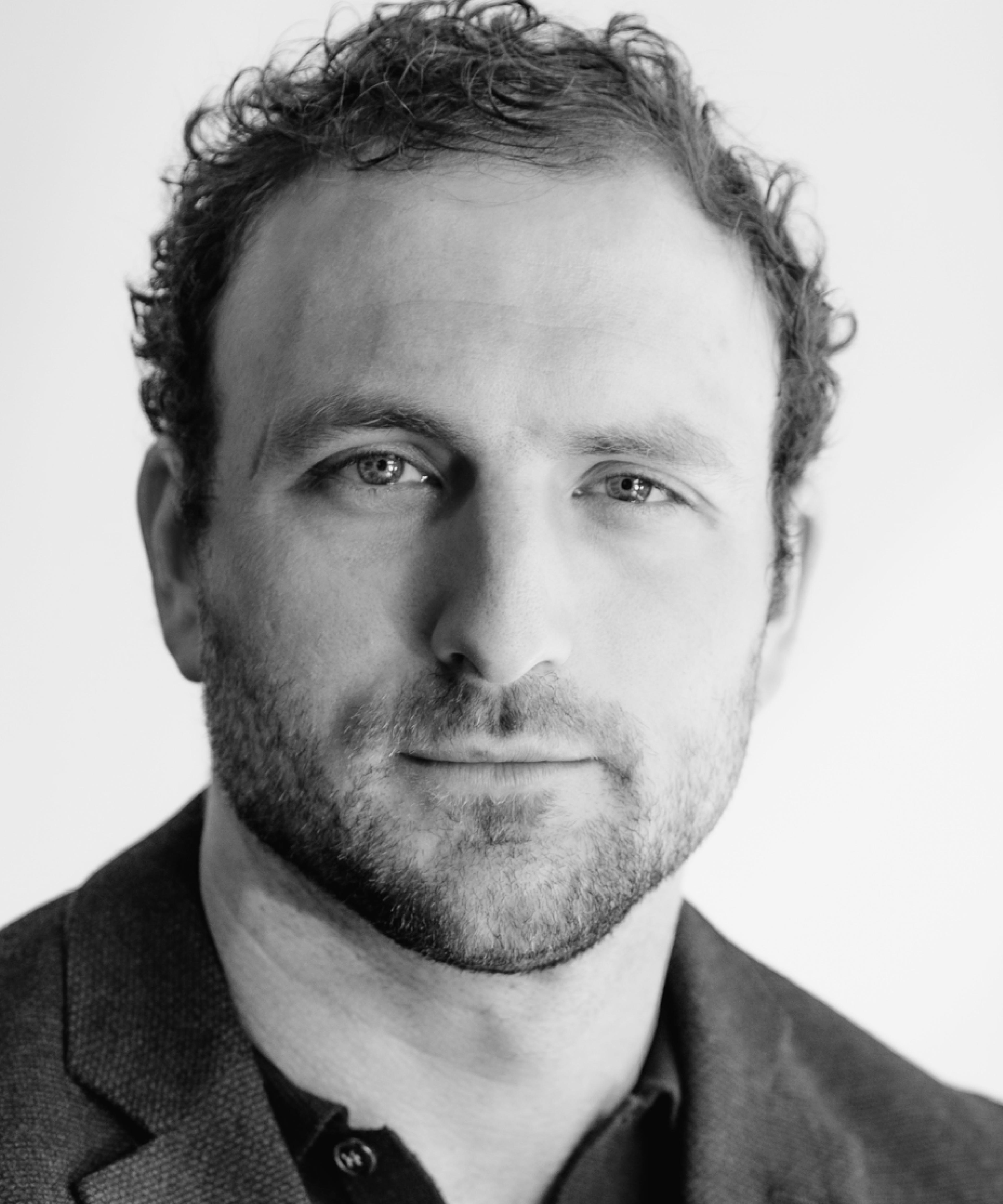 Portrait of Sam Allgood in a blue blazer against a white sunny background.
