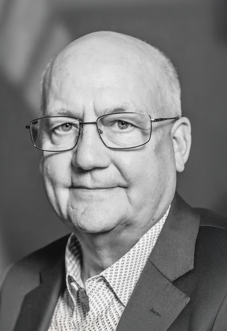 Black and white photograph of Duane Pfannenstiel, wearing thin-rimmed clear glasses and looking into the camera lens