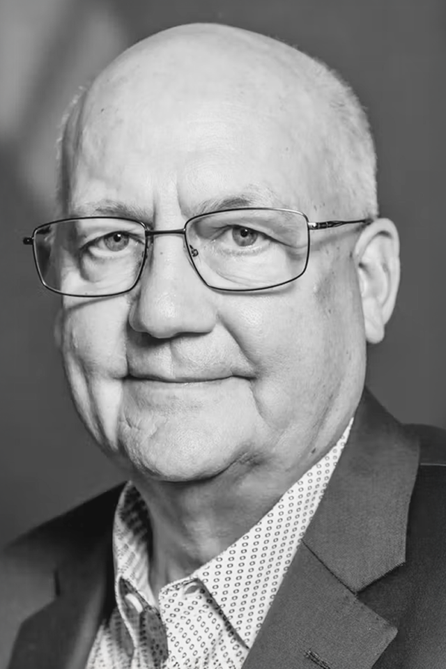 Black and white photograph of Duane Pfannenstiel, wearing thin-rimmed clear glasses and looking into the camera lens
