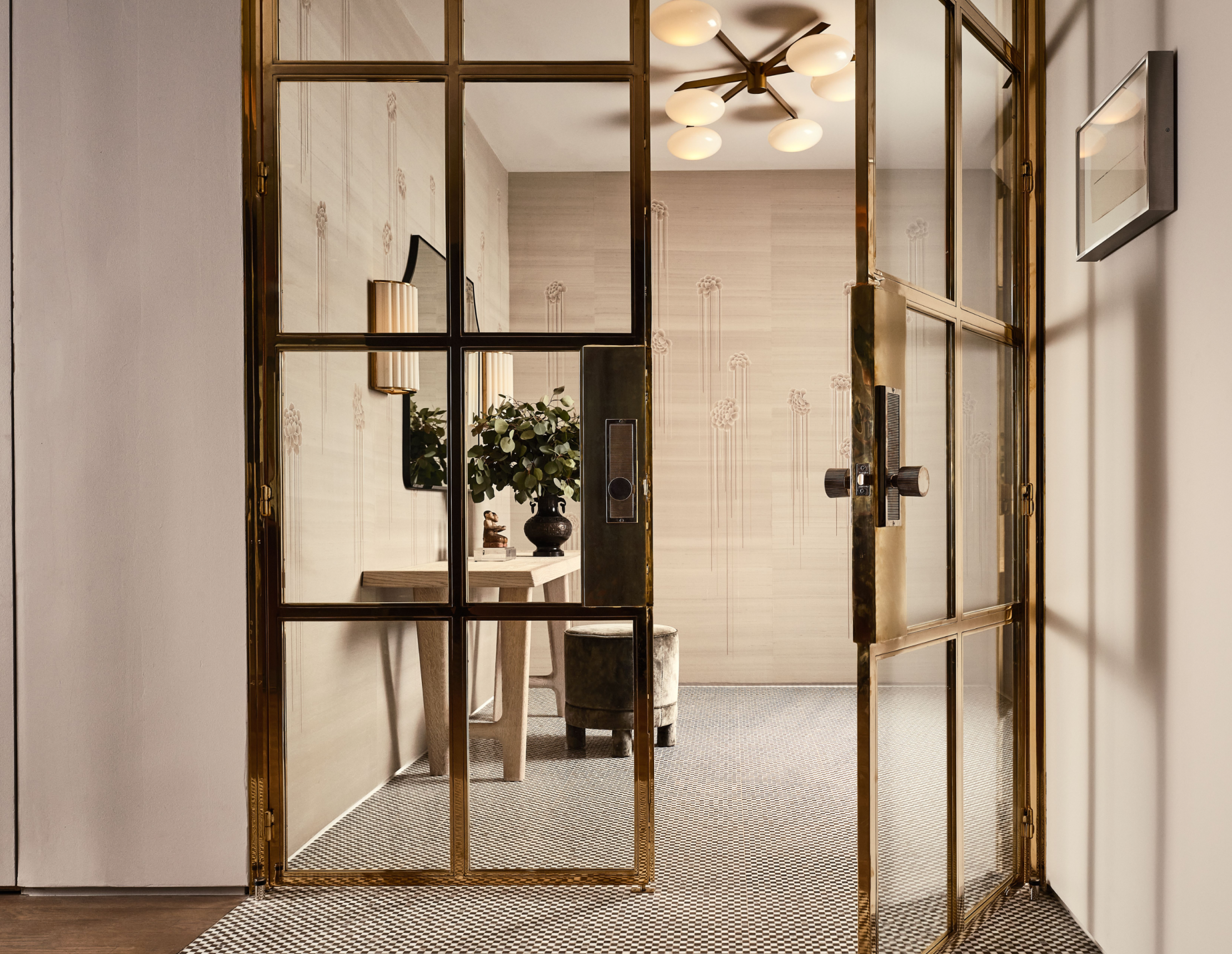 Brass doors with glass panes leading into a light colored hallway with monochromatic wallpaper