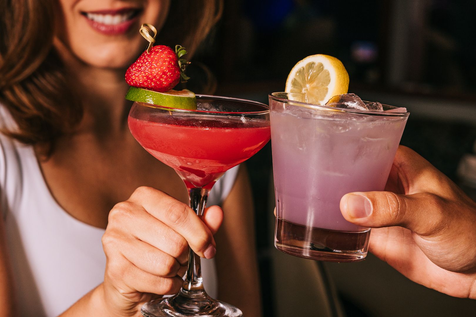 Woman and man raising a Strawberry Burlesque Daiquiri and Lychee White Linen cocktail.