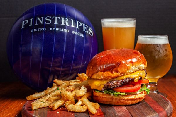 Bowling ball with Pinstripes logo next to two beers, a burger, and fries on a table