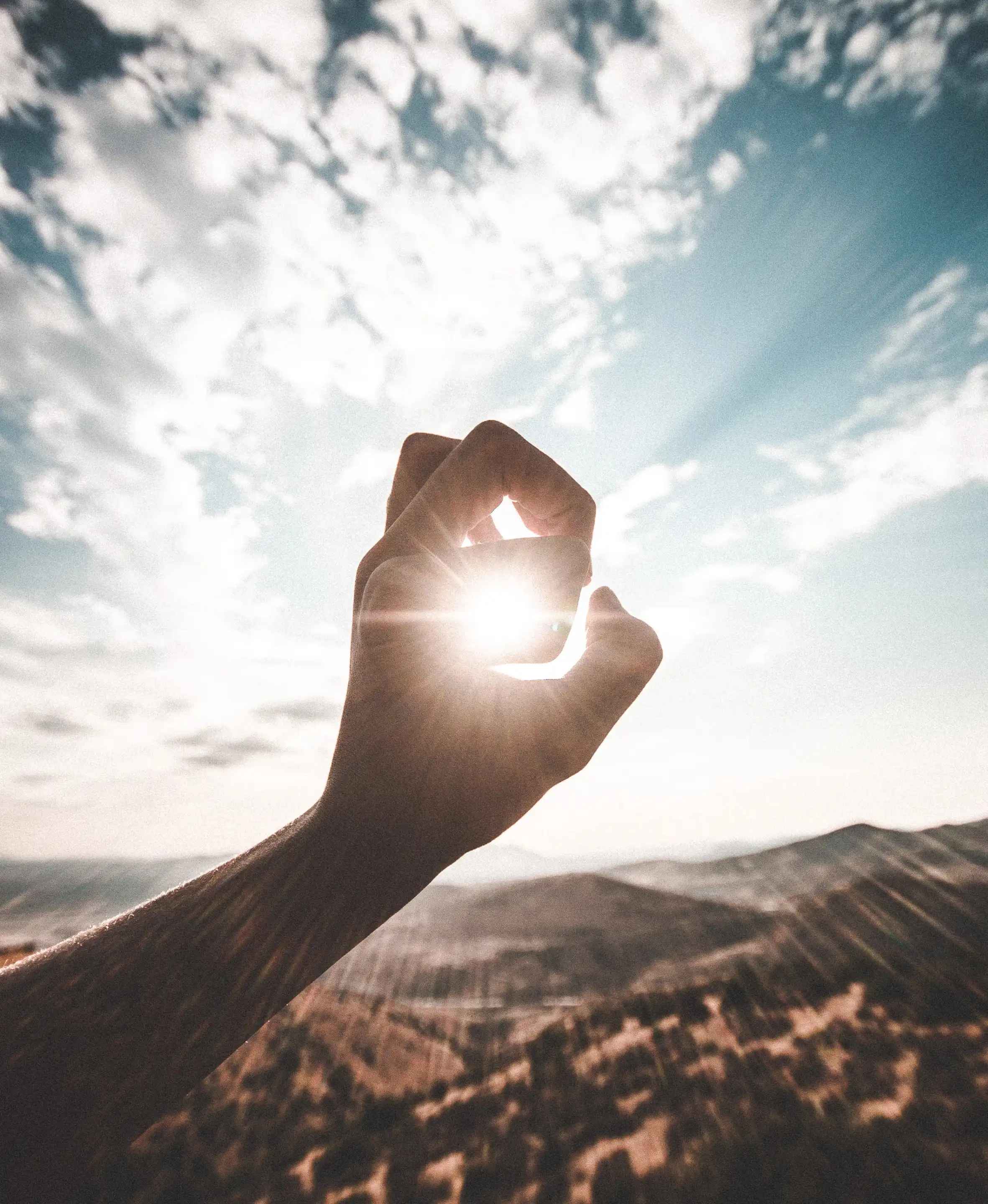 person forming an "O" shape around the sun hovering in a partially cloudy sky over a desert-like environment