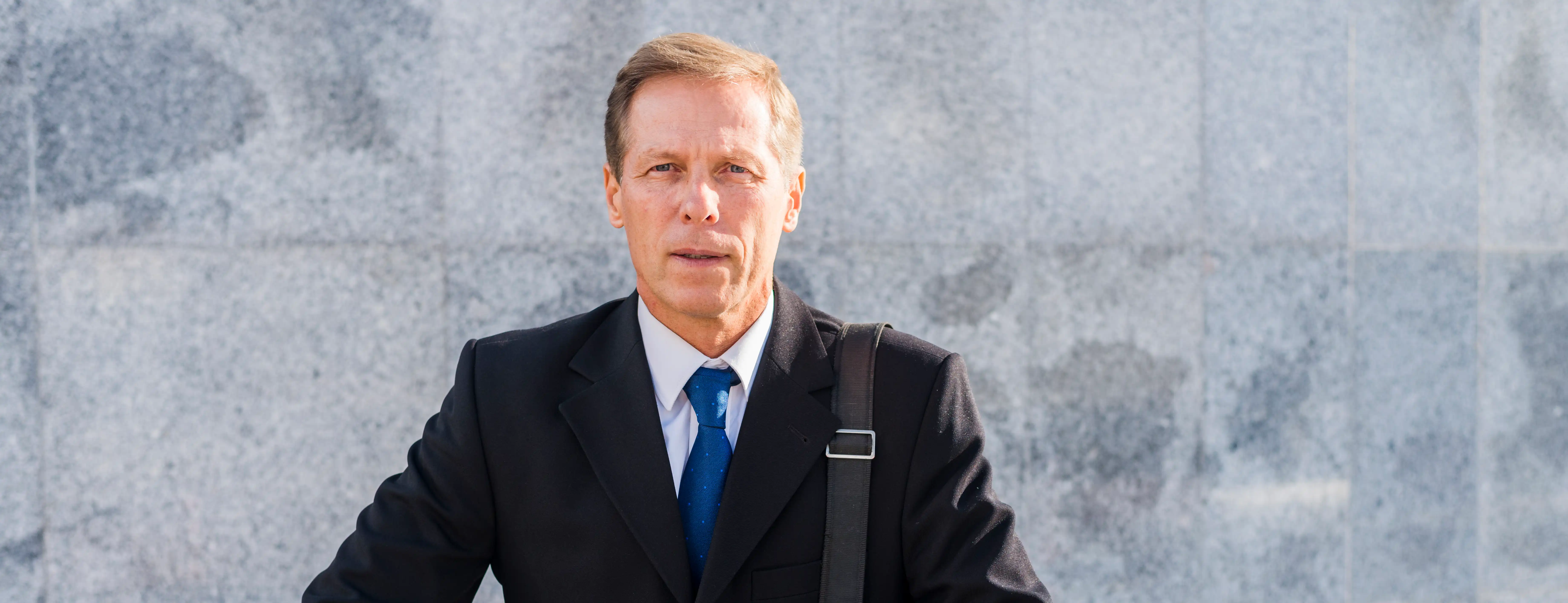 portrait of older businessman with hands on rails while wearing black suit and blue tie