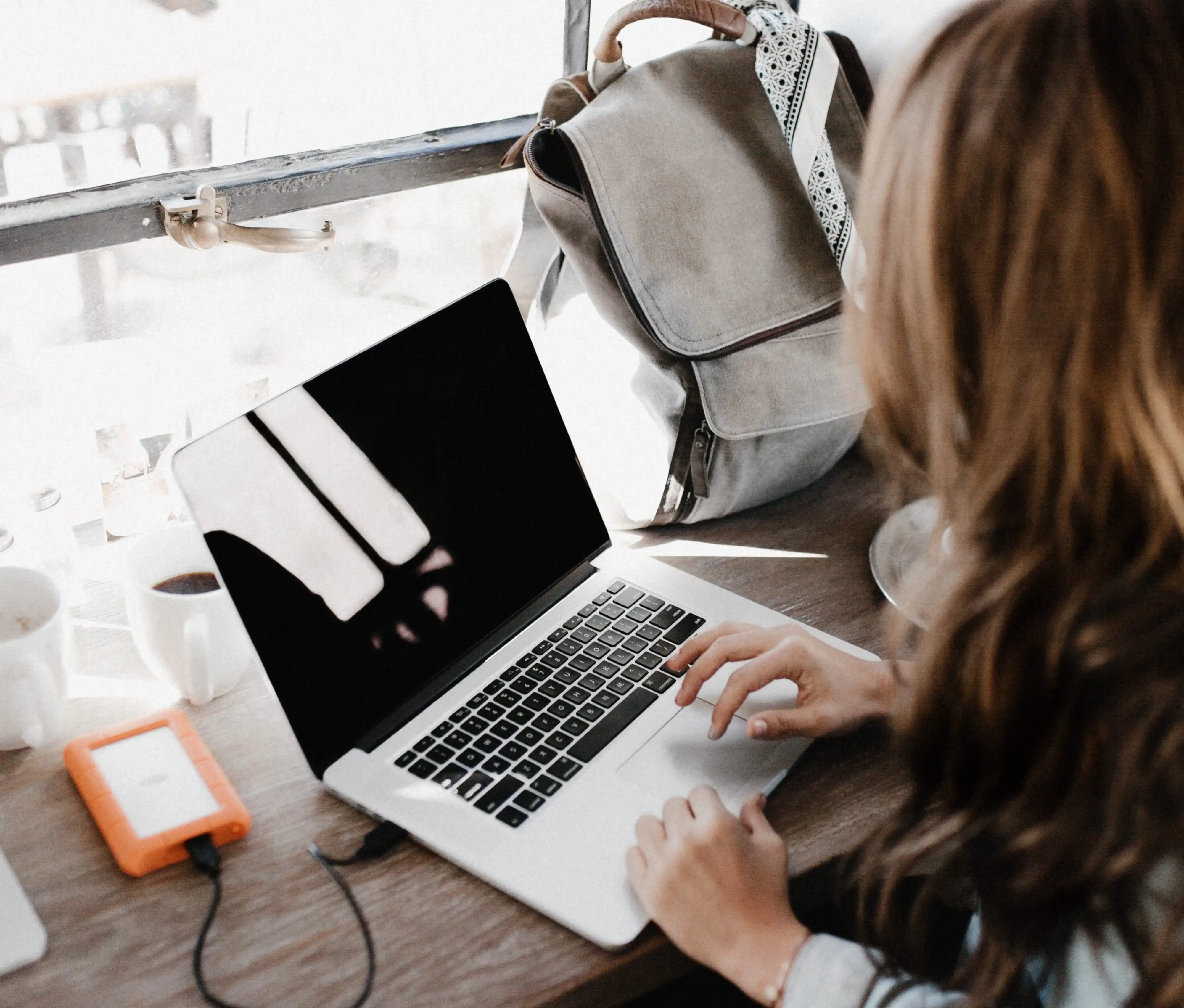 woman with brown hair with hand hover over touchpad of a laptop perched on sunlit desk