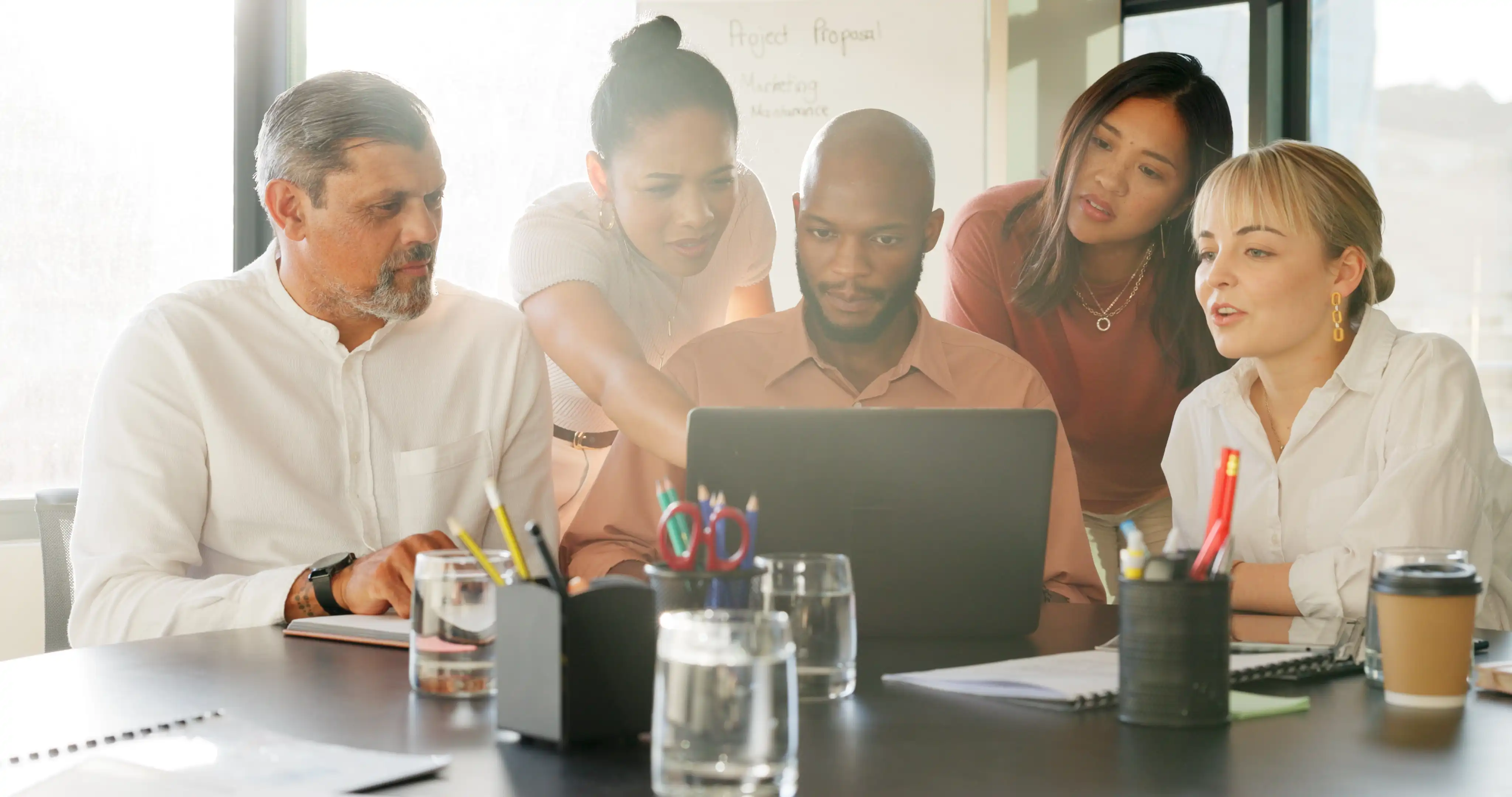coworkers collaborating with each other over in front of an open laptop in a sunlit work lounge