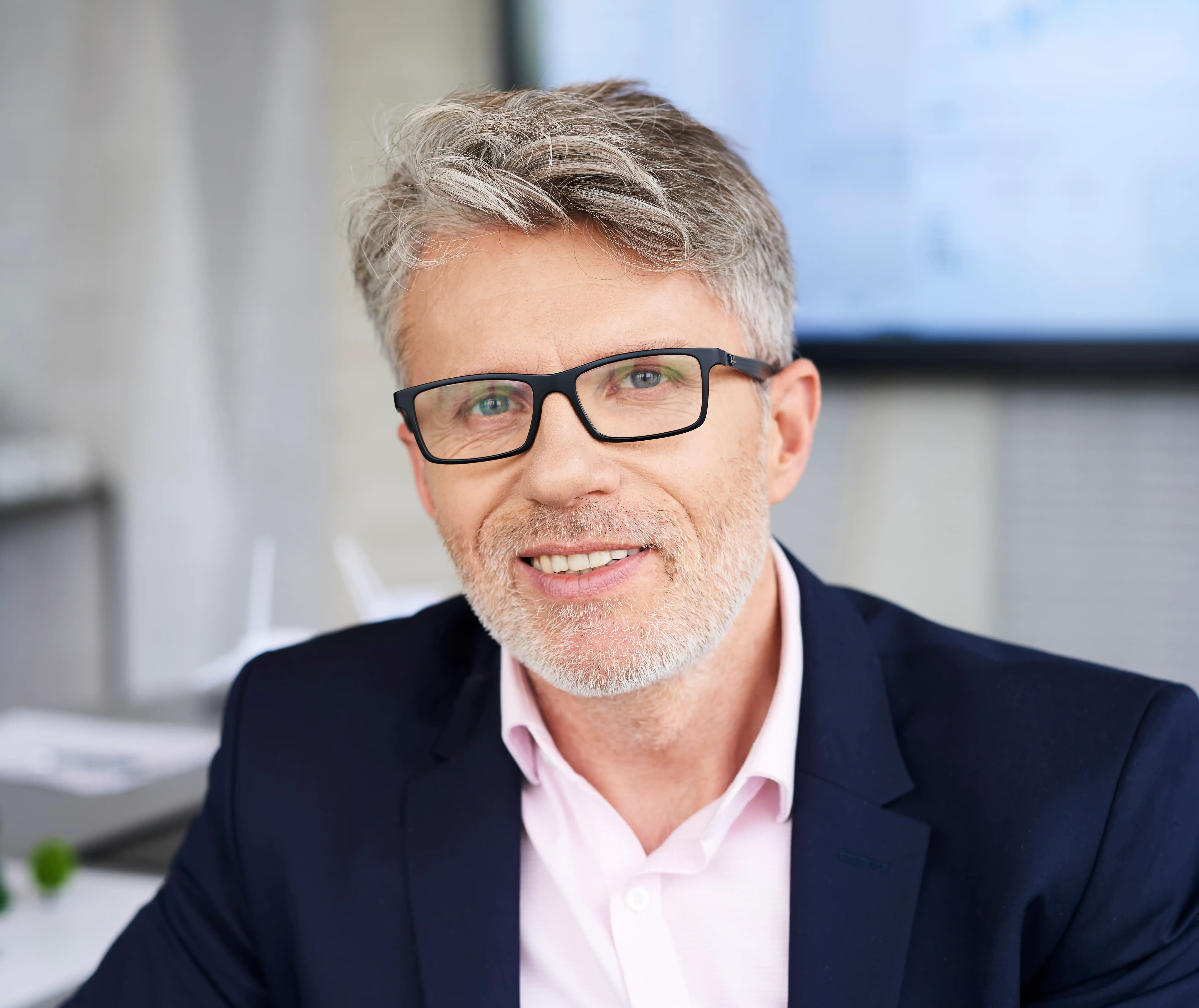Older professional man wearing glasses and a dark blue suit with a light pink shirt