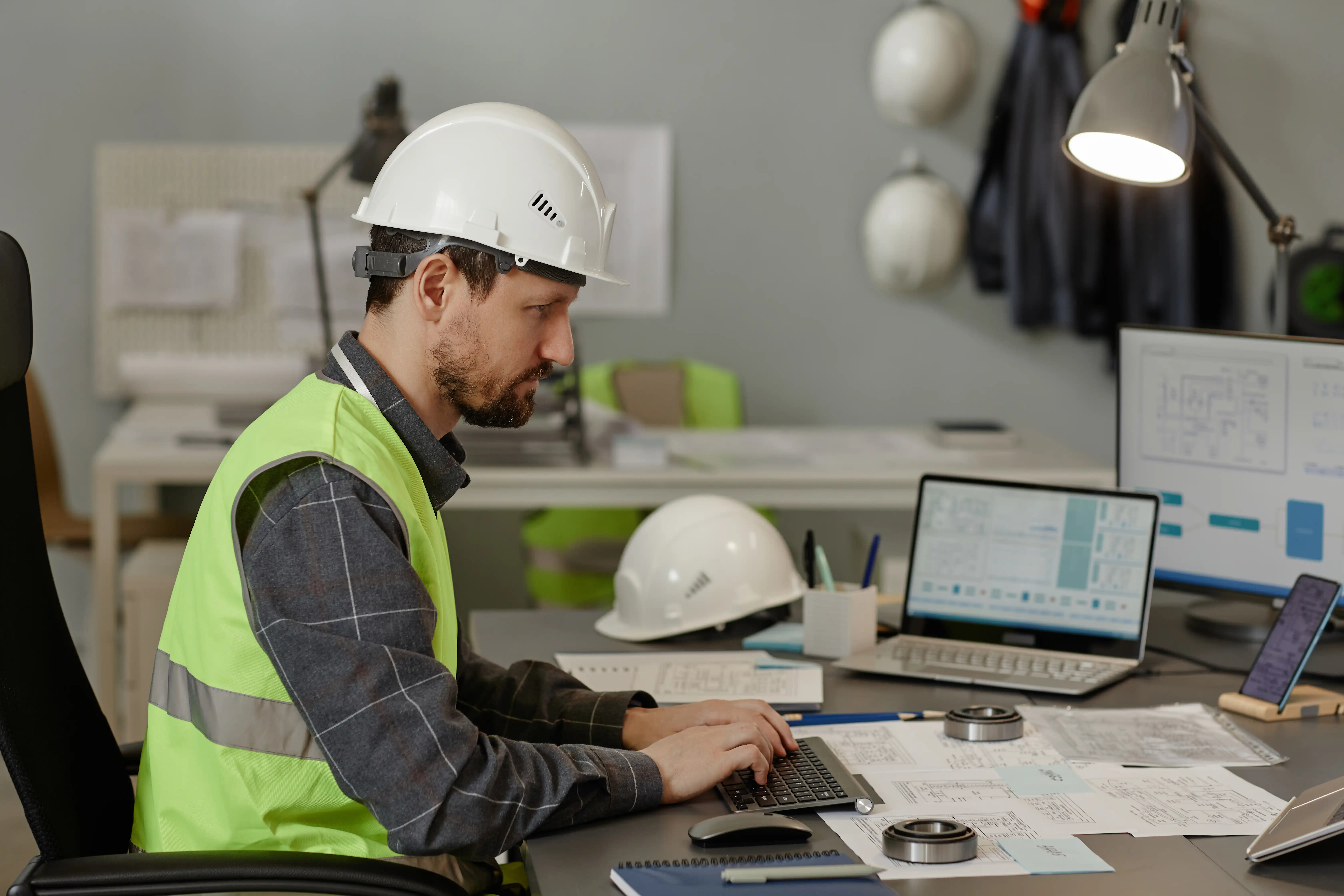 Engineer wearing hardhat at workplace in office and using computer devices