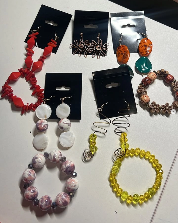 A flat lay of handmade beaded earrings and bracelets in coral, amber, teal, mother-of-pearl, and golden-yellow glass beads