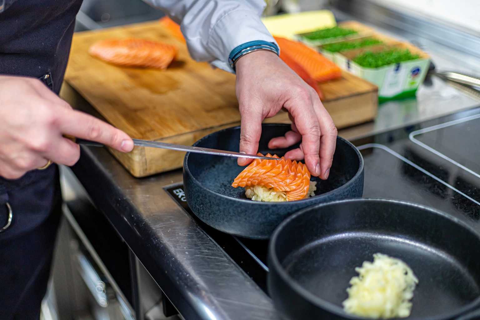 A chef precisely arranges intricately cut salmon in a bowl, showcasing the artistry of culinary preparation.