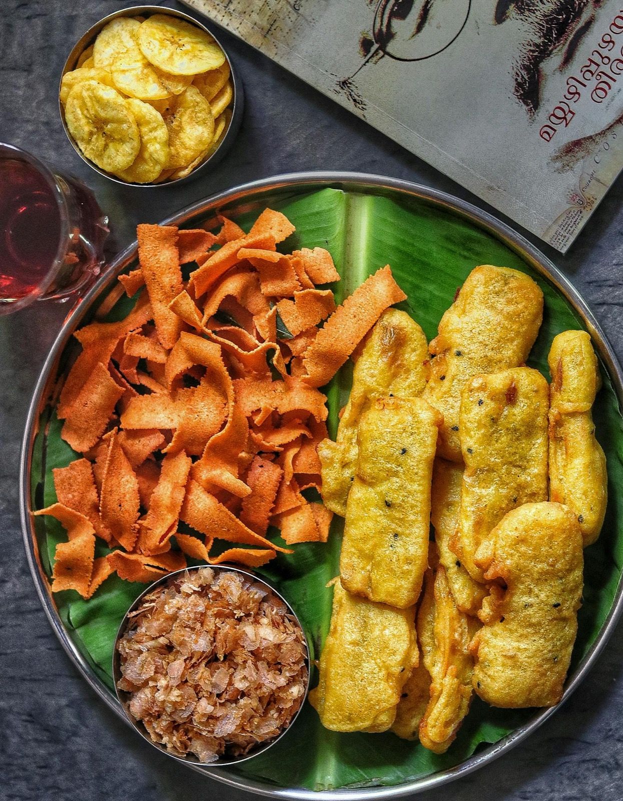 A beautiful overhead shot of Kerala snack platter on a banana leaf — tapioca chips, banana chips, and traditional South Indian snacks
