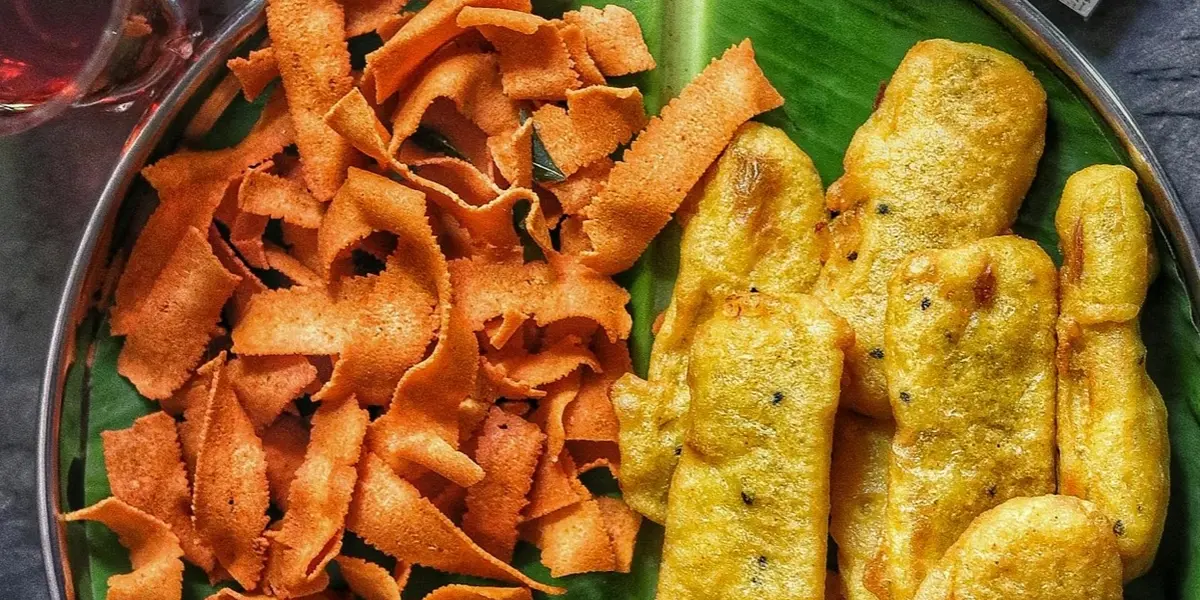 A beautiful overhead shot of Kerala snack platter on a banana leaf — tapioca chips, banana chips, and traditional South Indian snacks
